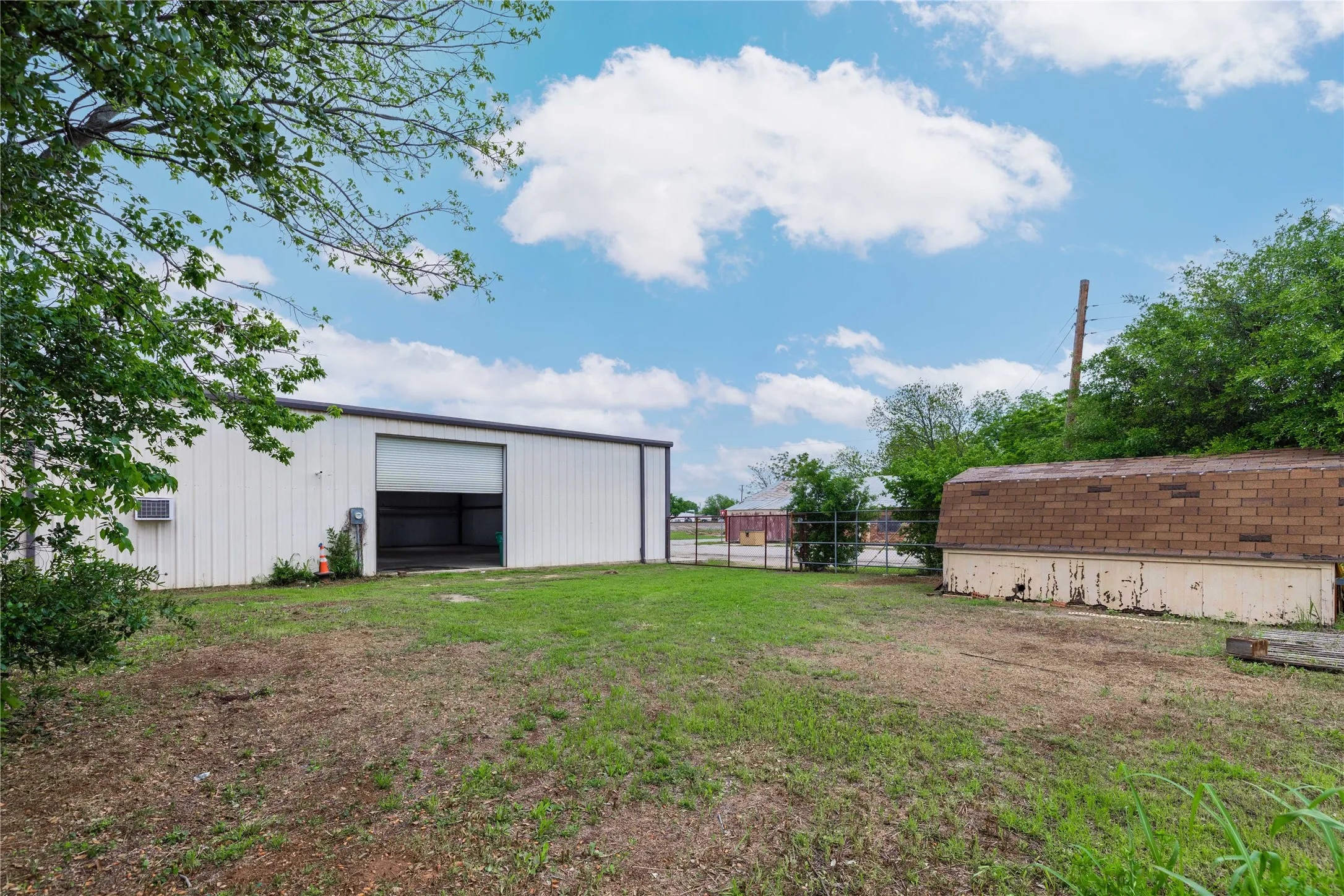 The property features a spacious metal building with a roll-up door, set on a lot with a grassy area