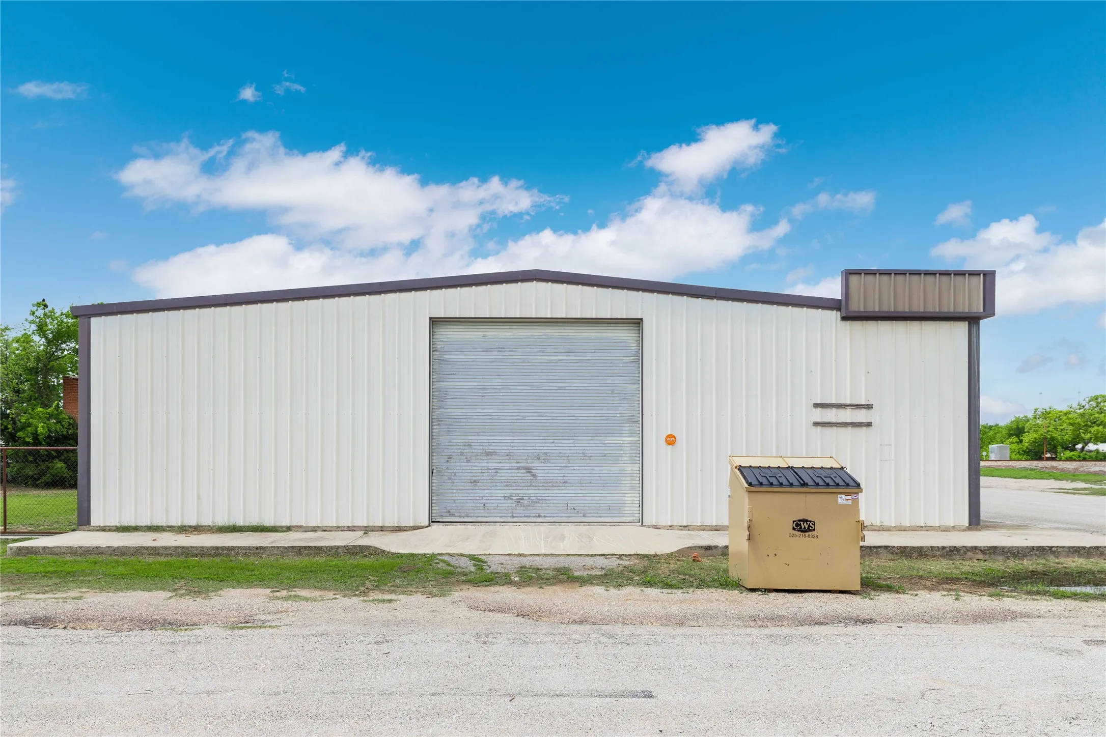 The property features a white metal building with a grey roll-up door, a dark grey trim, and a concrete foundation