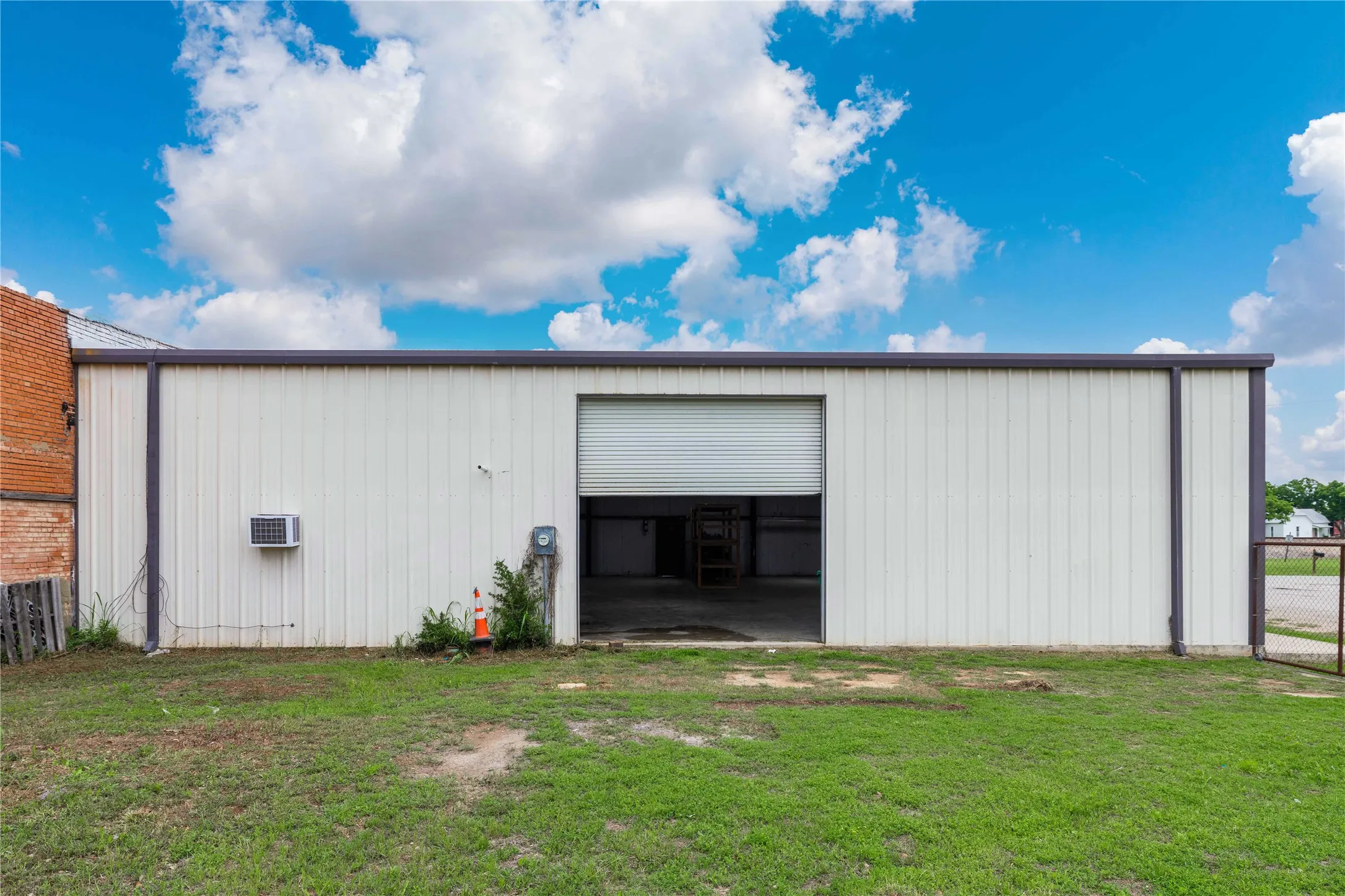 The property includes a large white metal building with a partially open garage door and an exterior air conditioning unit