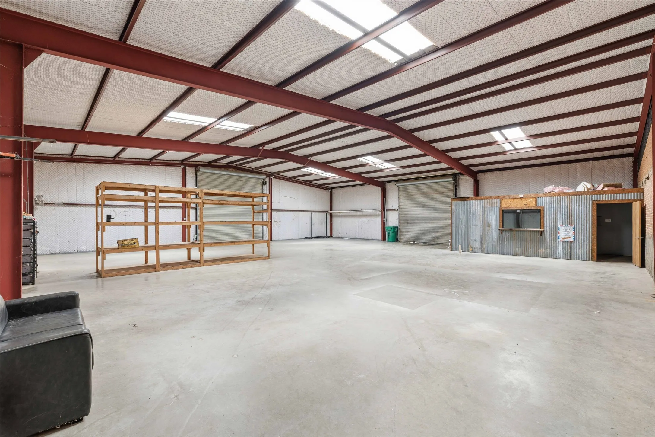 Expansive interior space featuring a concrete floor, exposed red metal beams, and skylights providing natural illumination