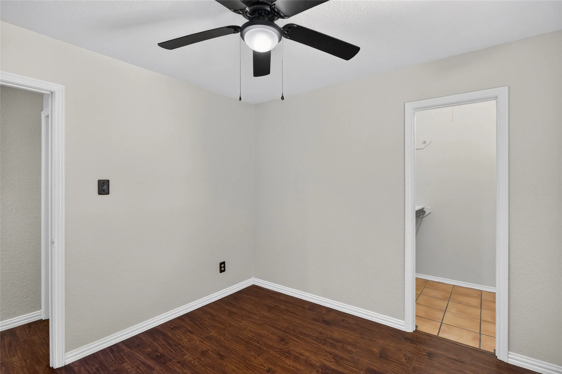 Room featuring wood-finish flooring, light neutral wall paint, and a ceiling fan with integrated lighting
