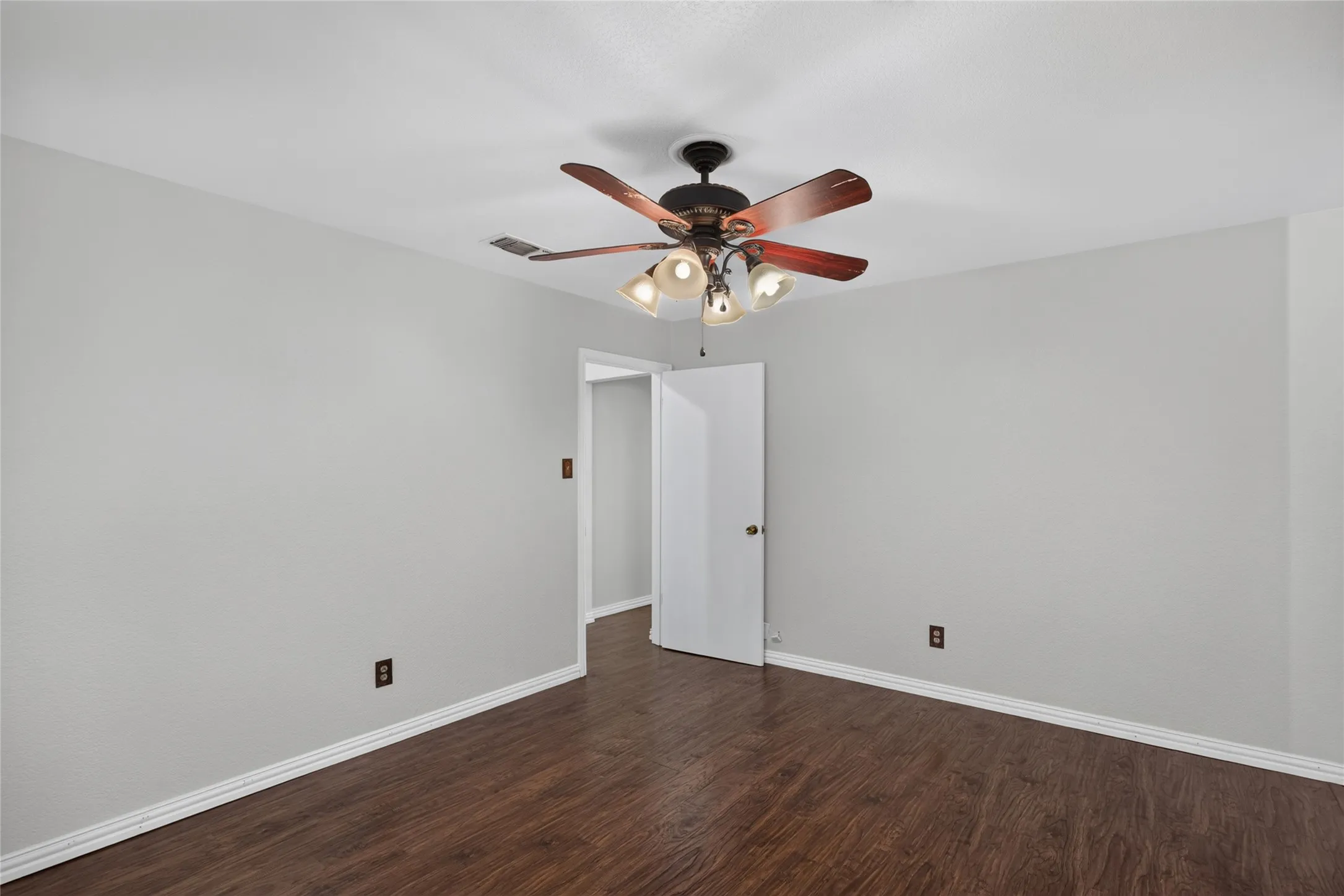 Room featuring wood-finish flooring, light grey painted walls, white baseboards, and a ceiling fan with integrated lighting