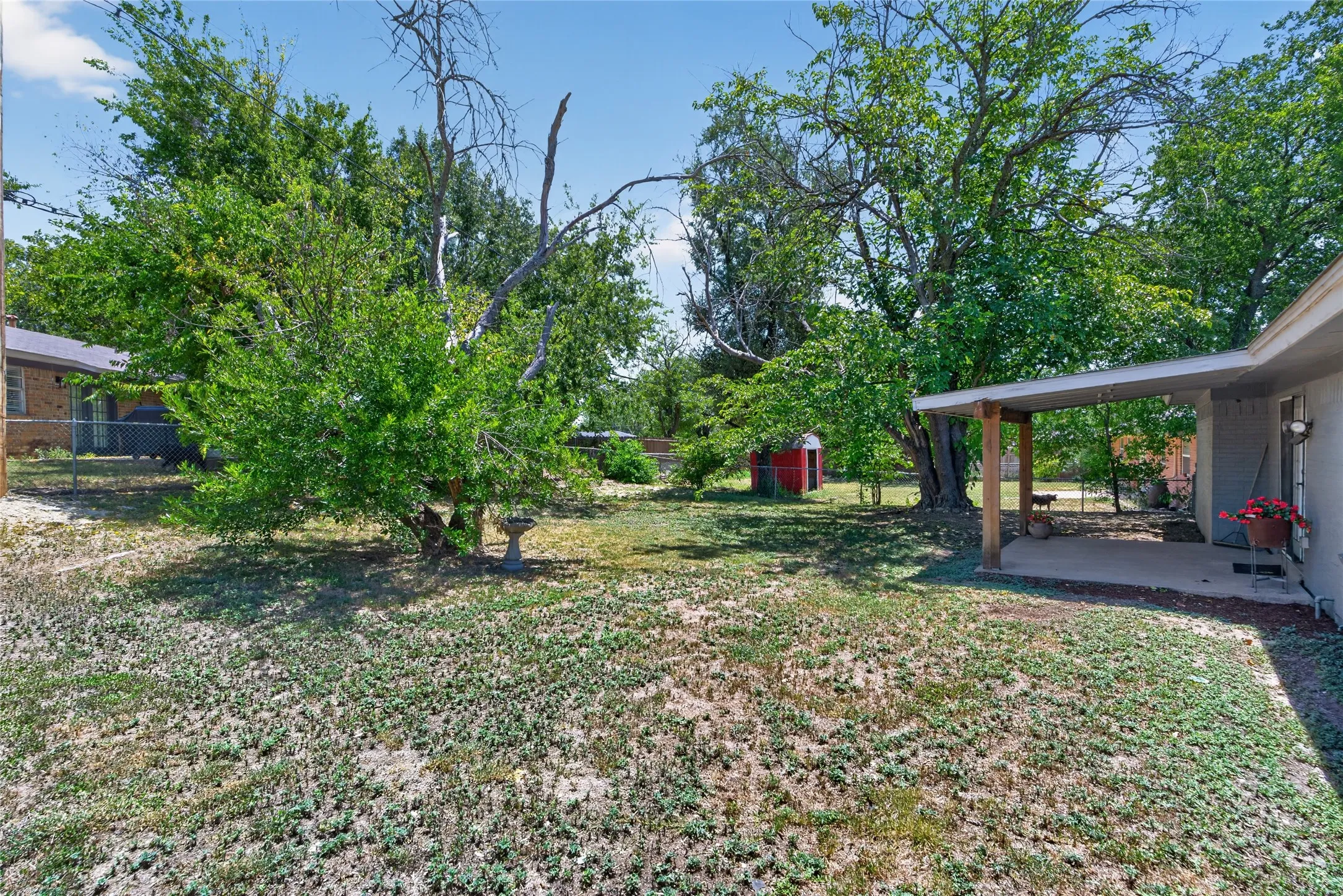 Spacious rear yard with mature trees and a covered patio area