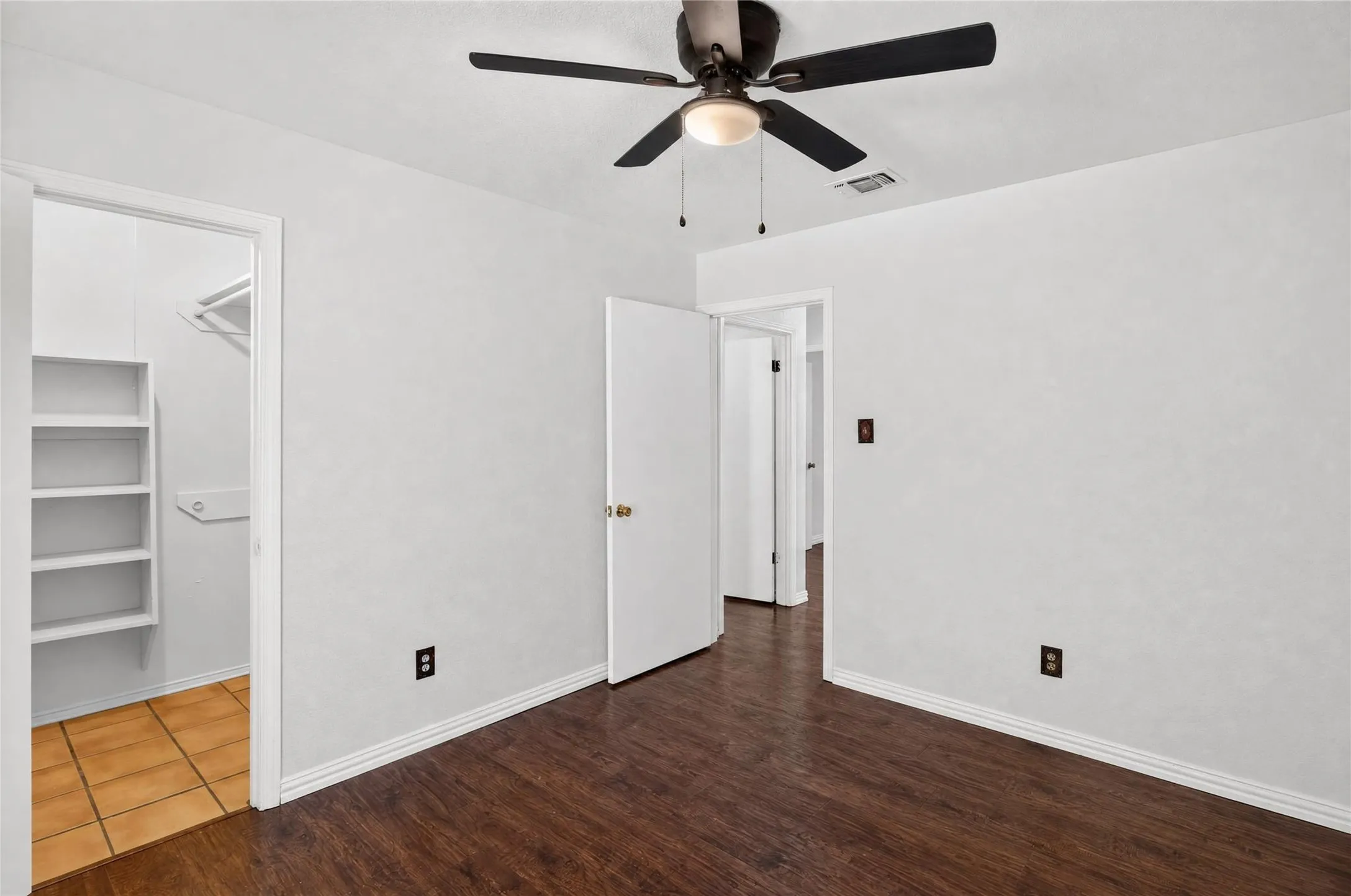 Bedroom featuring wood-finish flooring, a ceiling fan with integrated lighting, and a closet with built-in shelving and tile flooring