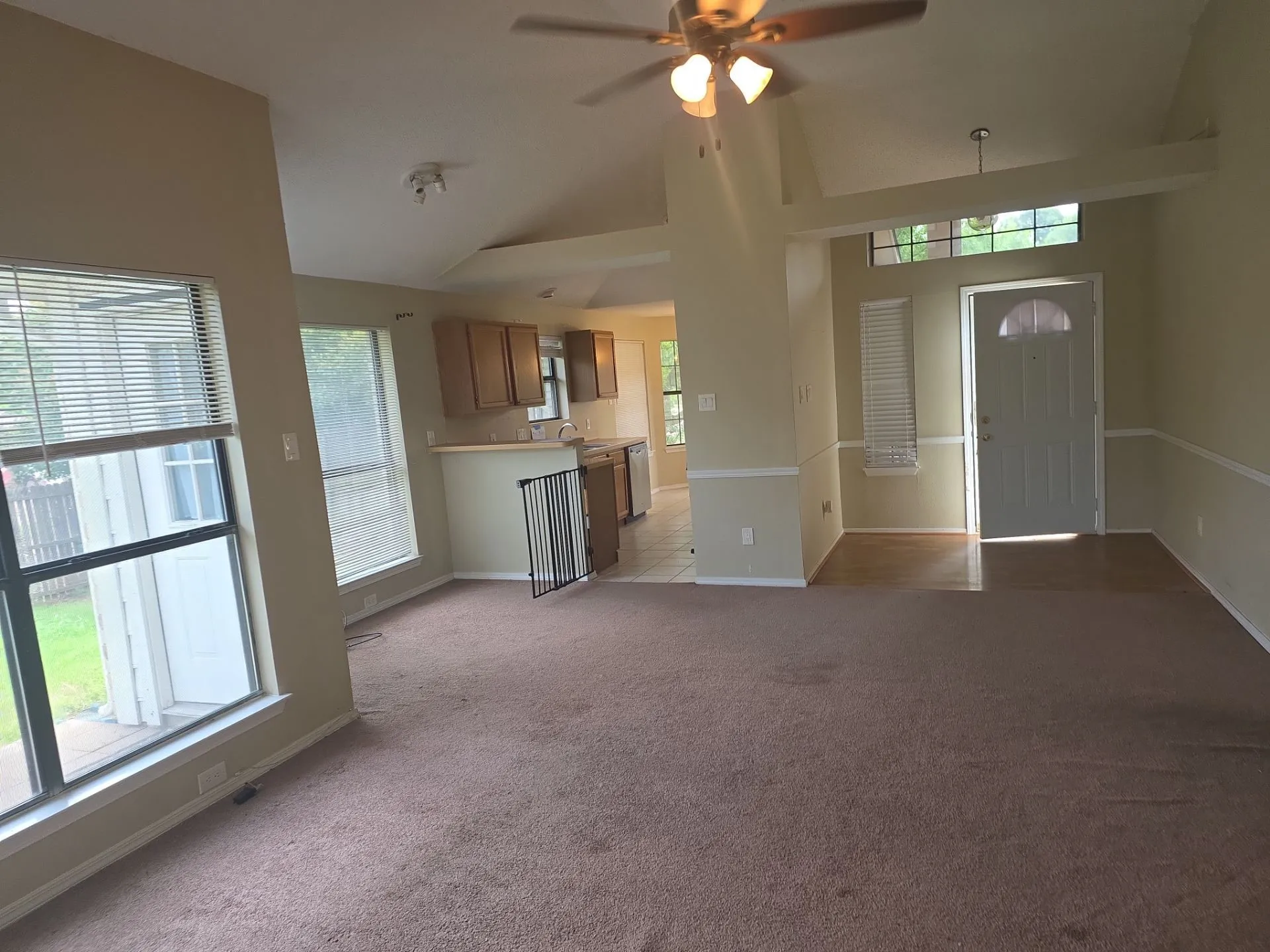 The property features a spacious living area with vaulted ceilings, a ceiling fan, and large windows with blinds for ample natural light
