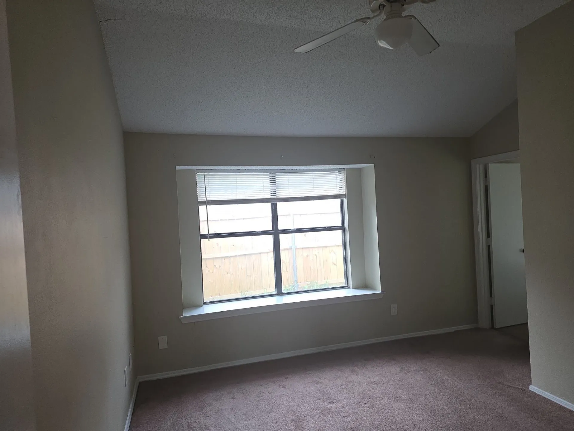 This room features a window with blinds, a ceiling fan, and carpeted flooring