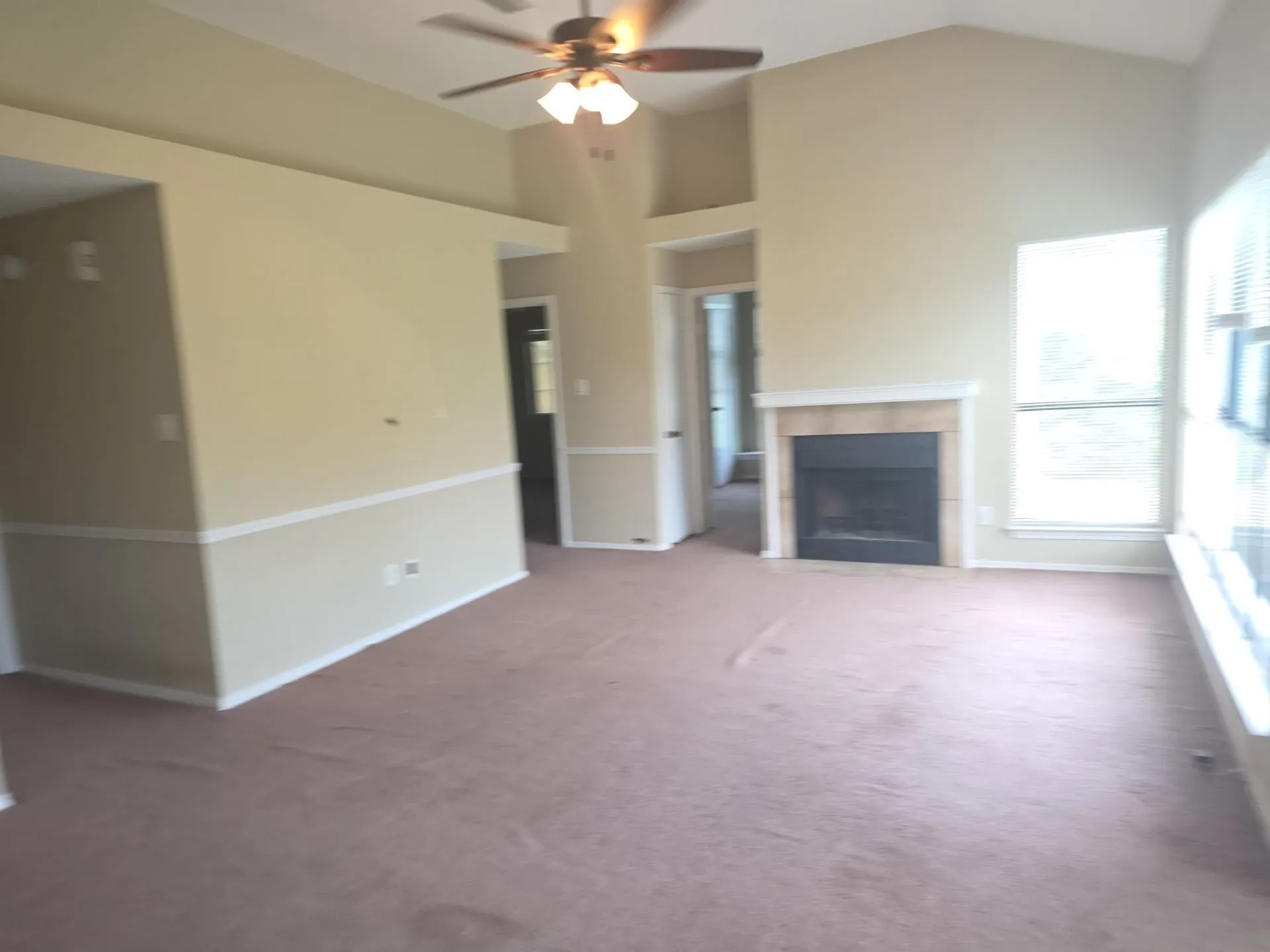 Living area featuring vaulted ceilings, a ceiling fan, a fireplace with a mantel, and a window with blinds