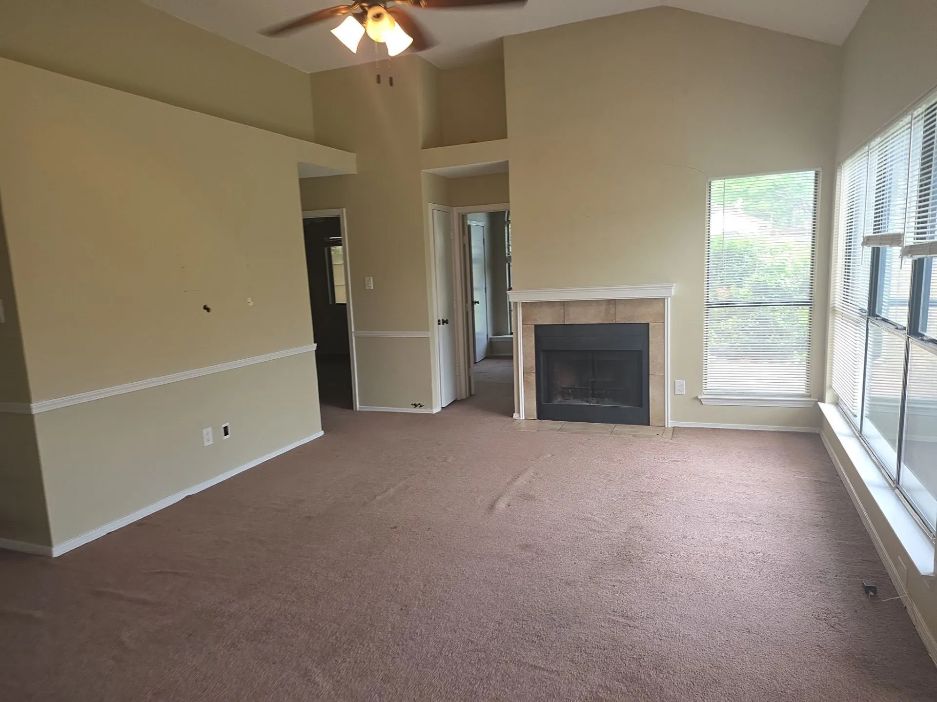 Spacious room featuring vaulted ceilings, a ceiling fan with integrated lighting, and carpeted flooring
