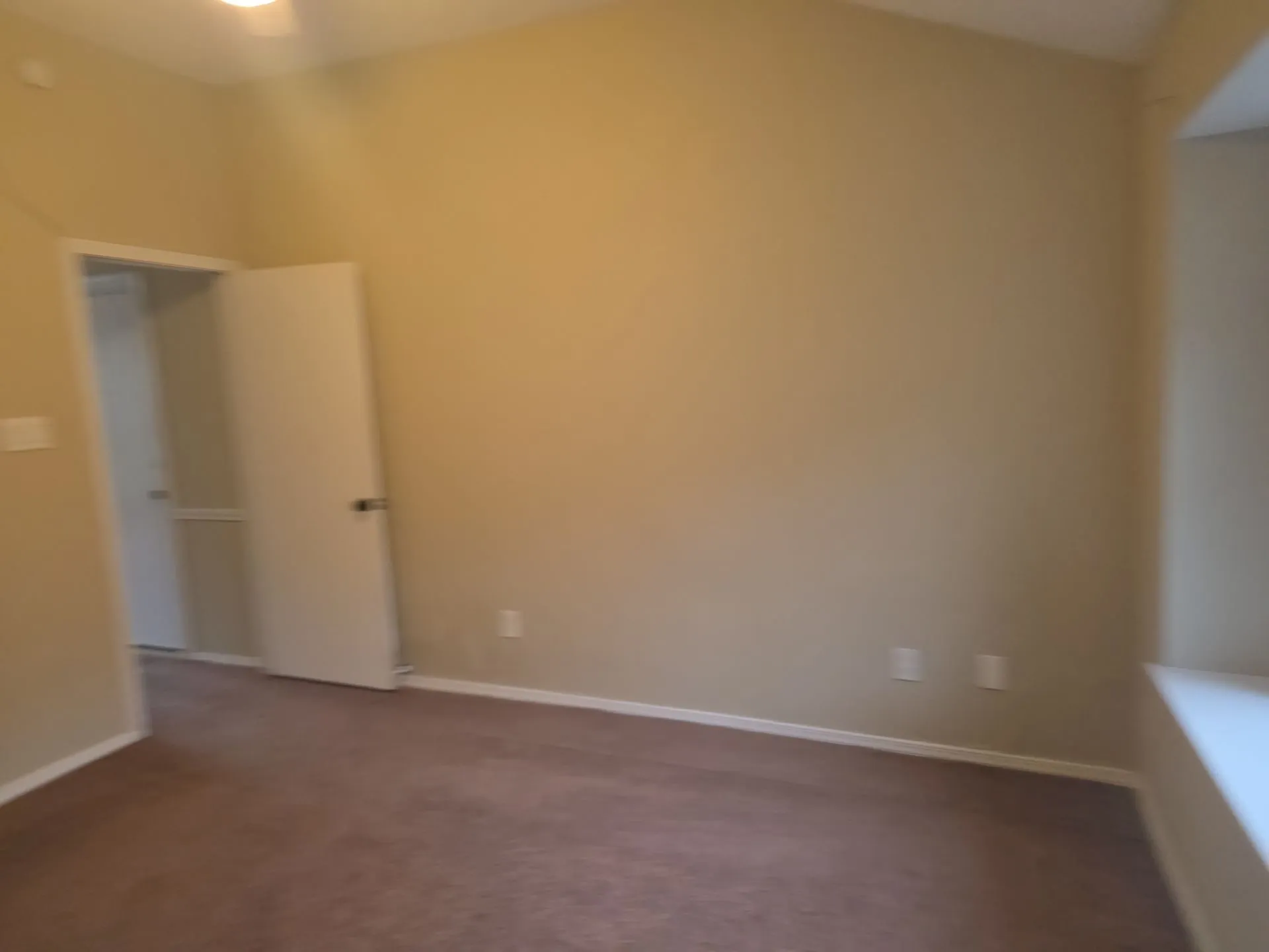 This room features a vaulted ceiling, light-colored walls, and brown carpeting