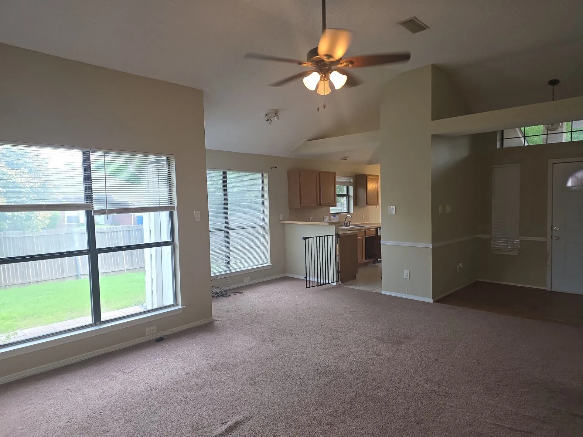 The property features a spacious living area with carpeted flooring, large windows providing natural light and views of the yard, and a ceiling fan