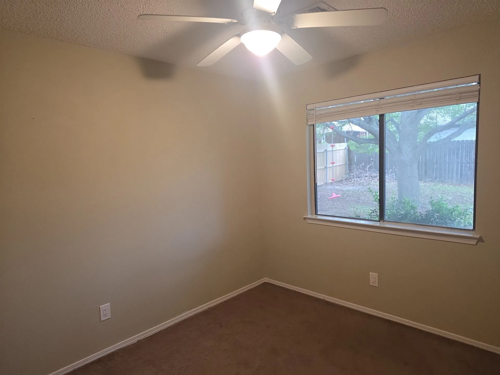 This room features a window overlooking the backyard, carpeting, and a ceiling fan