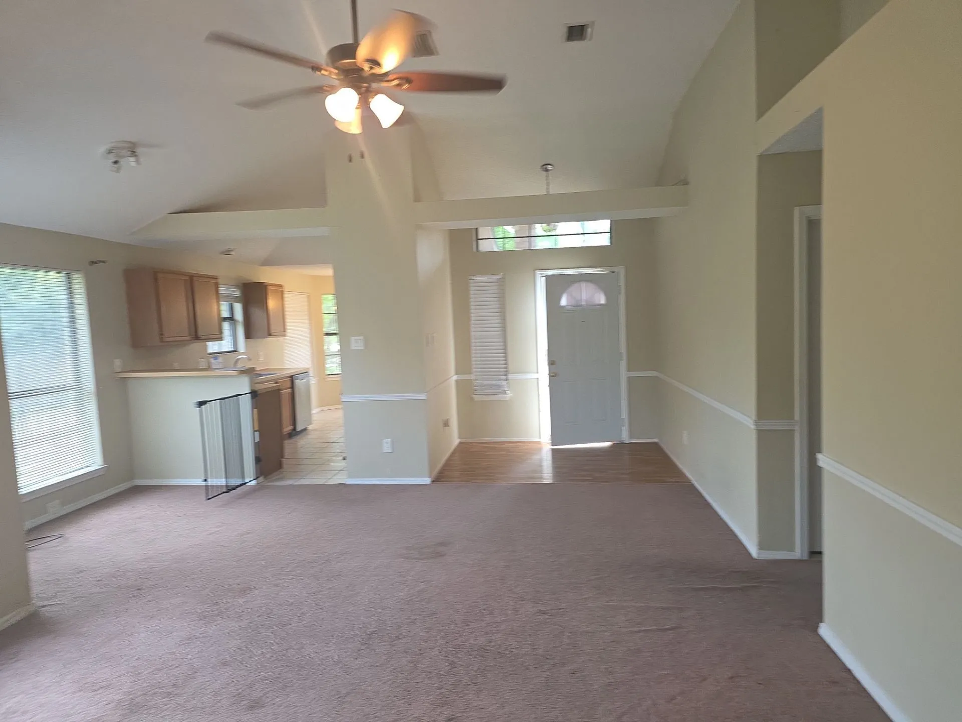 Living area featuring a ceiling fan with light fixture, vaulted ceiling, and carpeted flooring
