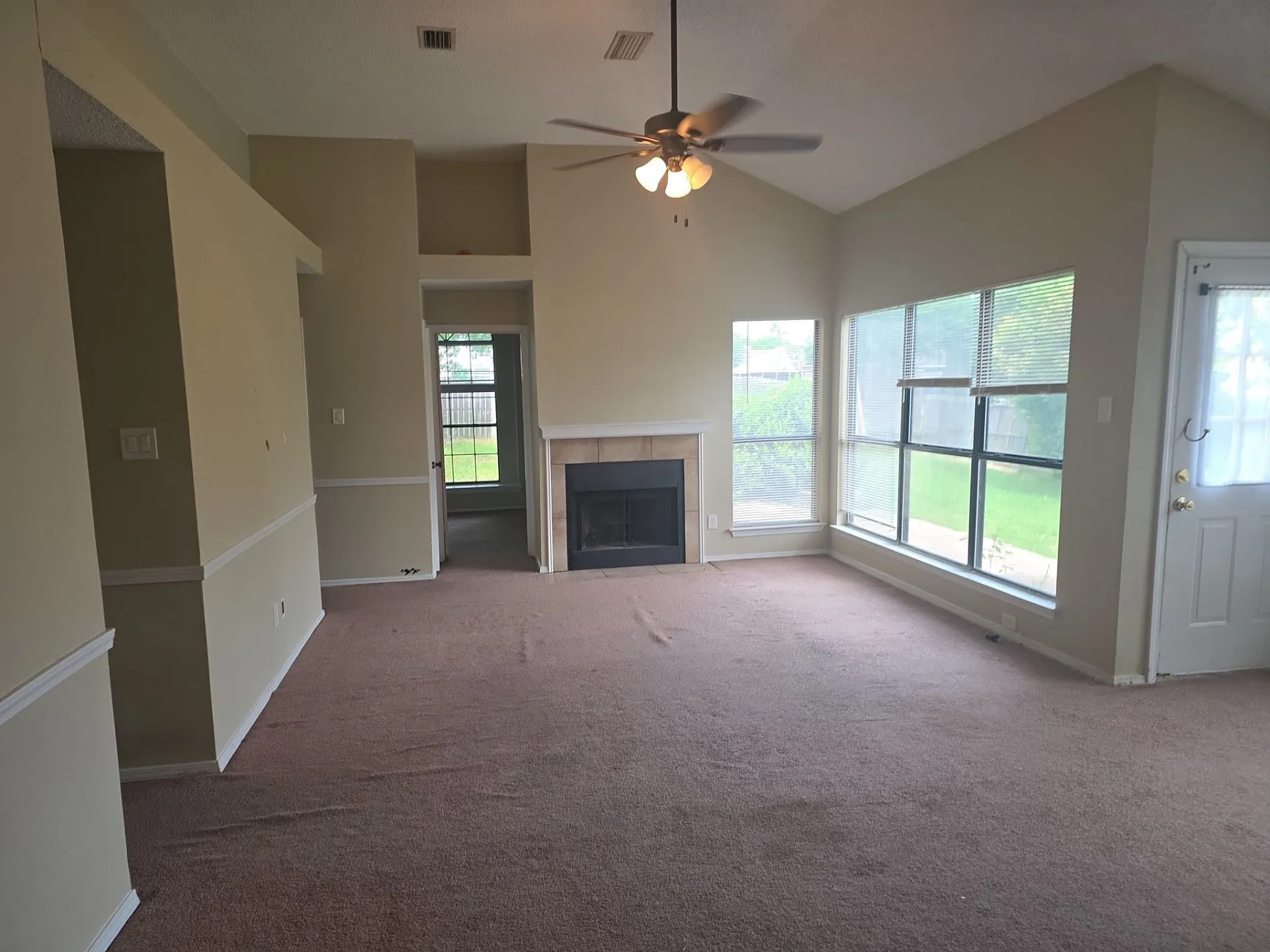Expansive living area with vaulted ceilings, a ceiling fan, and large windows providing natural light