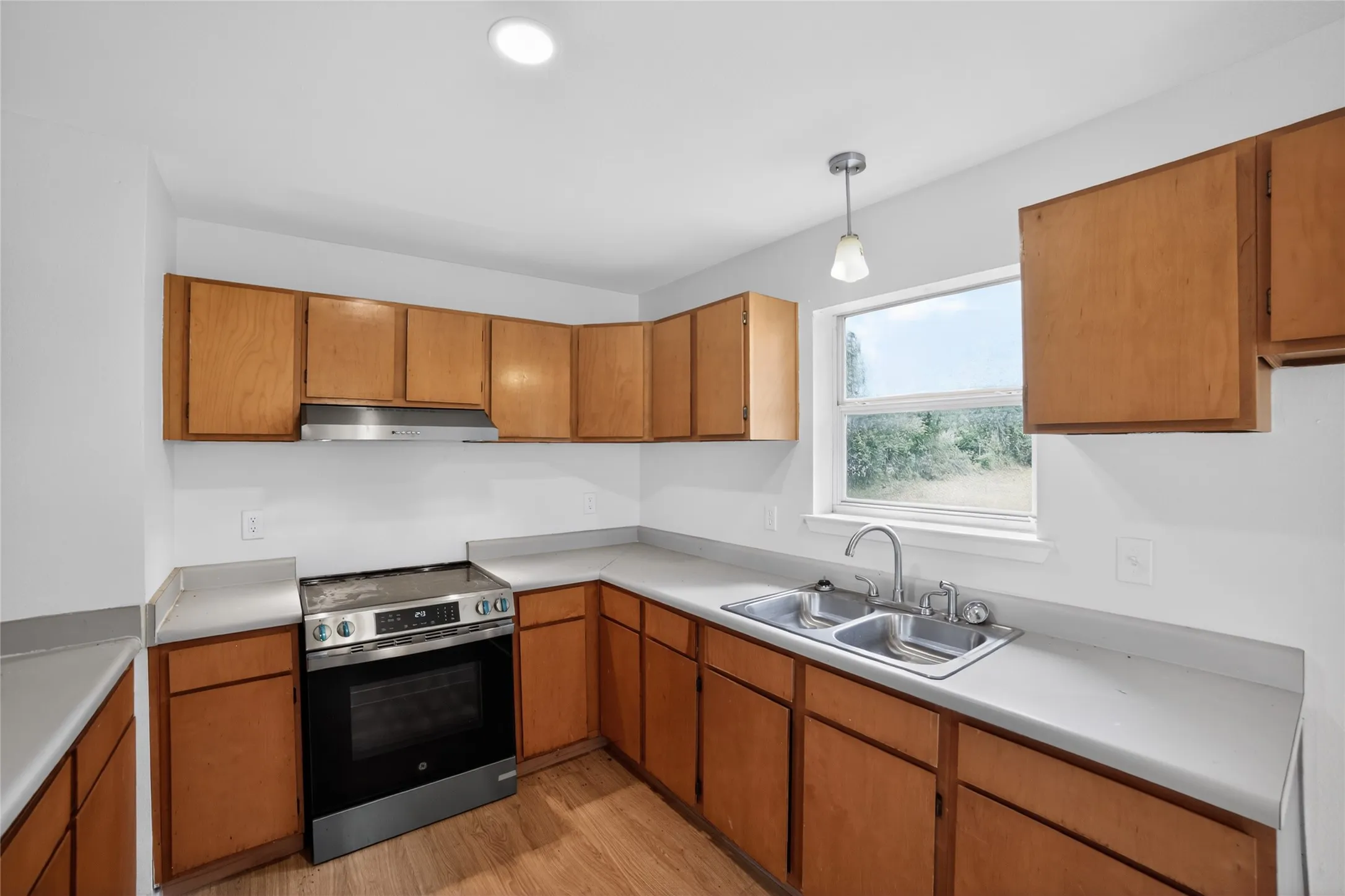 The kitchen features light wood cabinetry, a stainless steel range with a matching range hood, and a dual basin sink