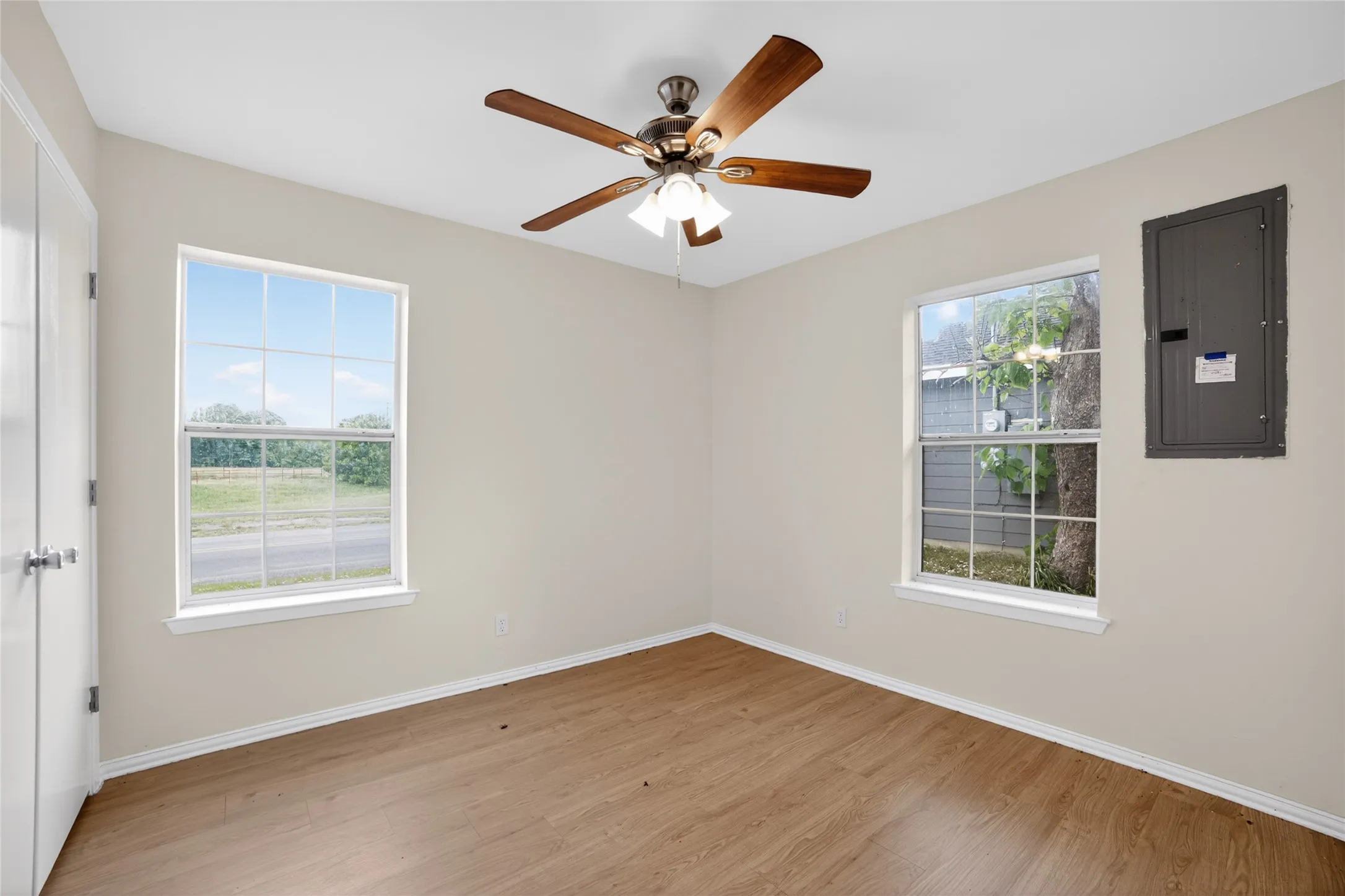 This room features light-colored walls, wood-style flooring, a ceiling fan with light fixture, and two windows