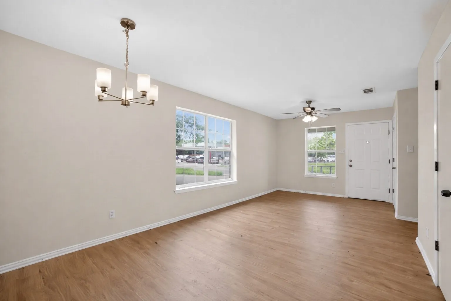 Spacious living area featuring light-colored walls, wood-look flooring, and a ceiling fan