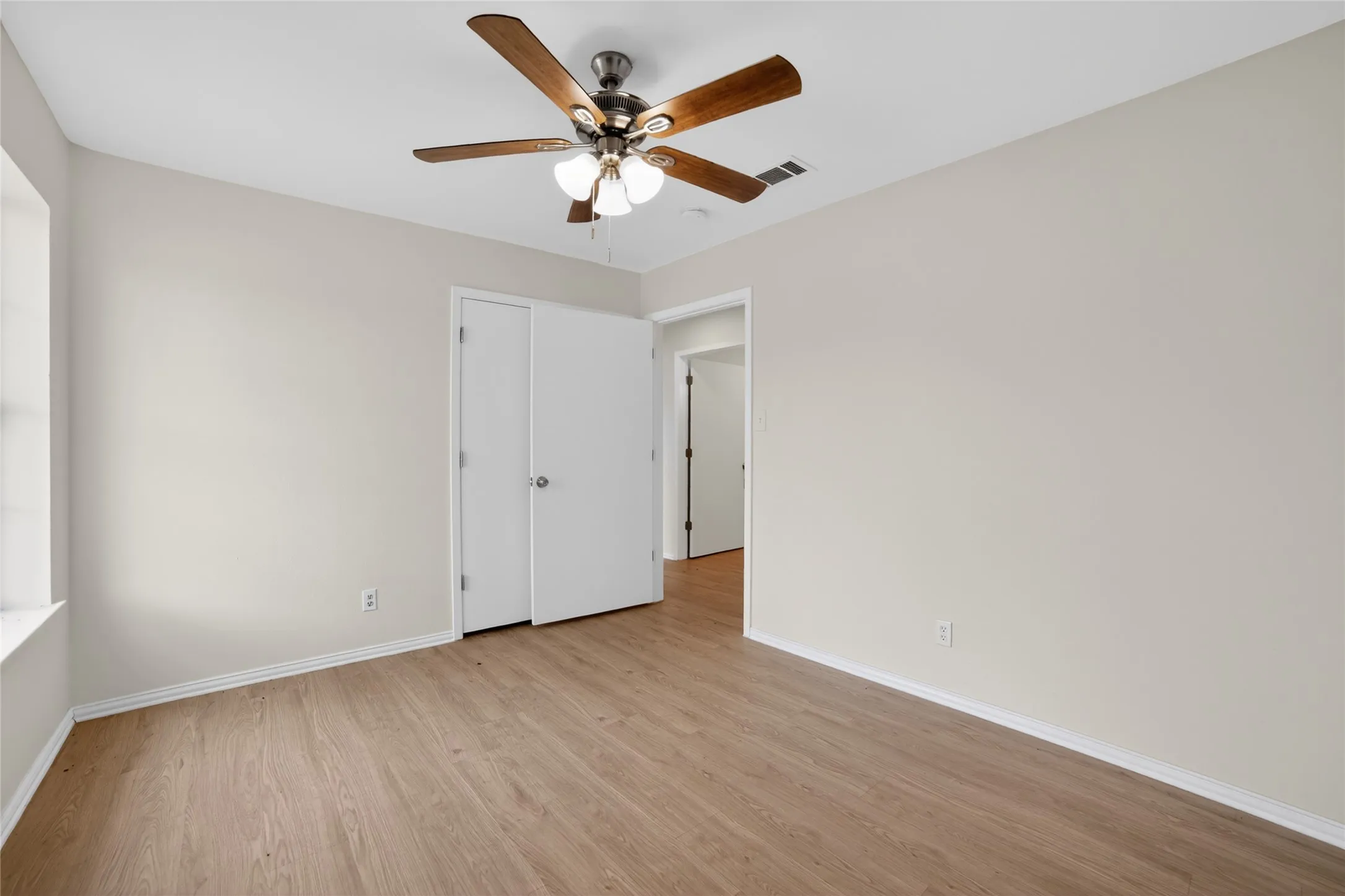This room features light-colored walls, wood-look flooring, and a ceiling fan with integrated lighting