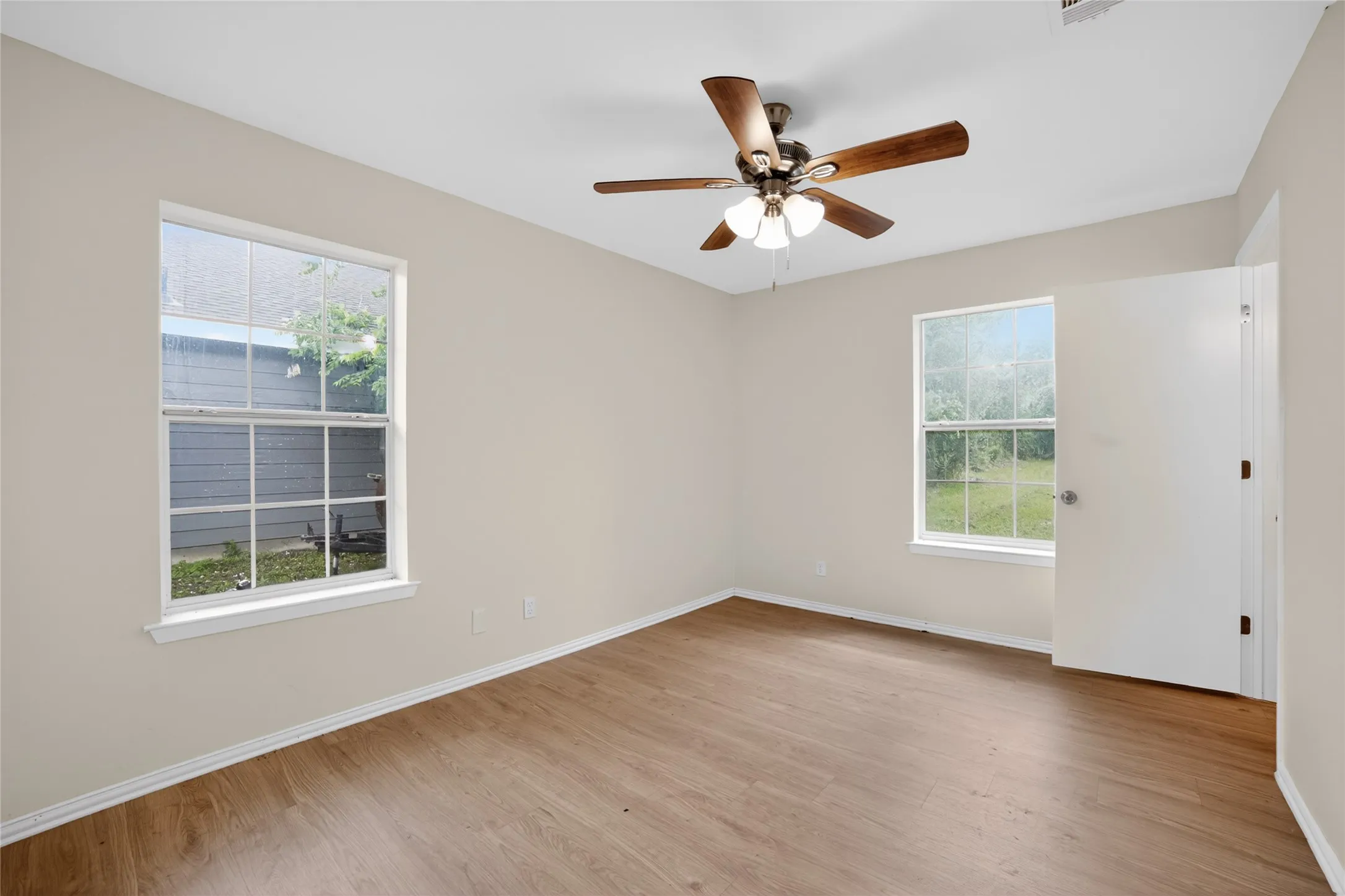 This room offers neutral walls, wood-look flooring, and a ceiling fan with light fixture