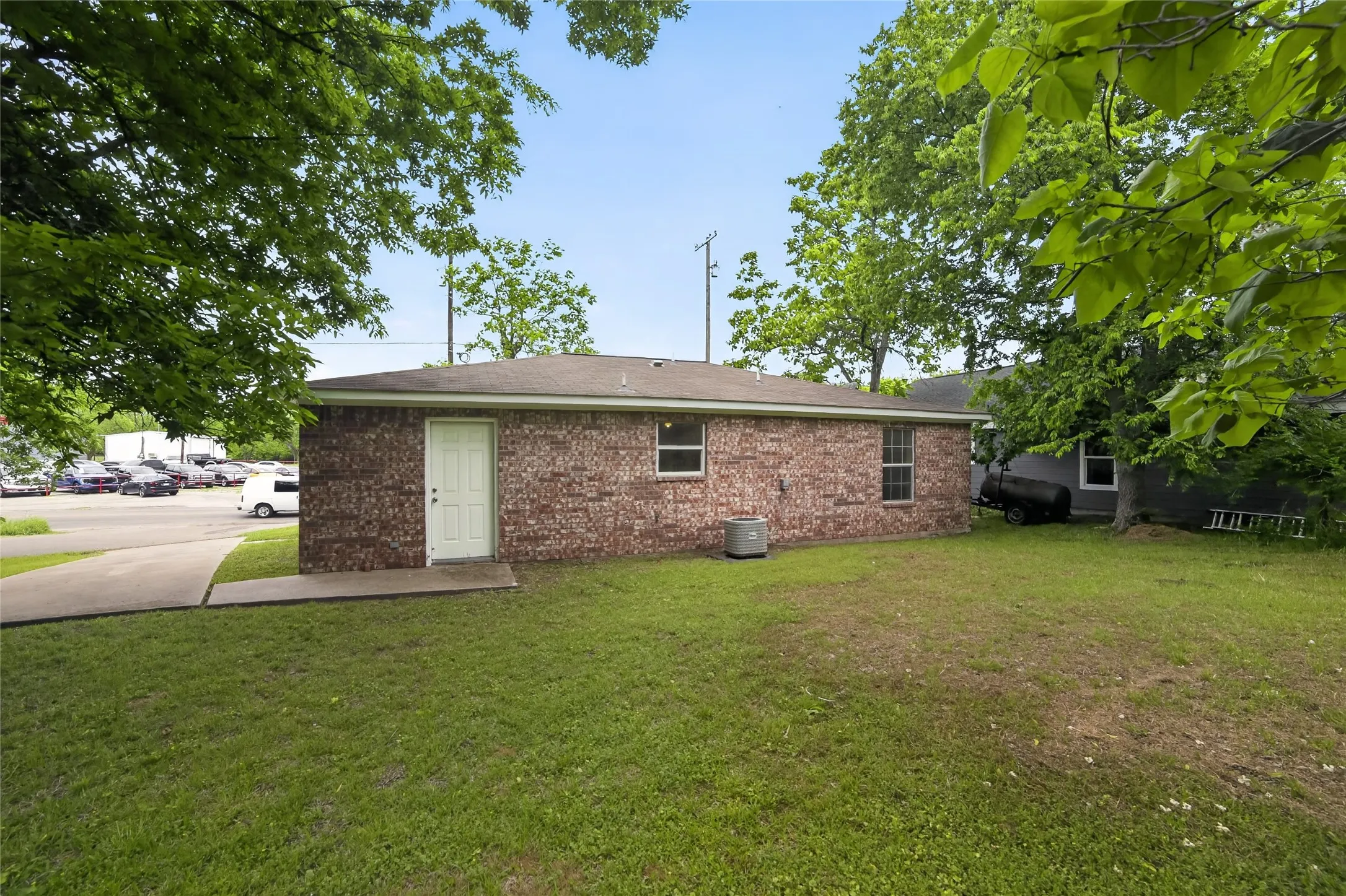 The property features a brick exterior, a well-maintained lawn, and mature trees providing shade