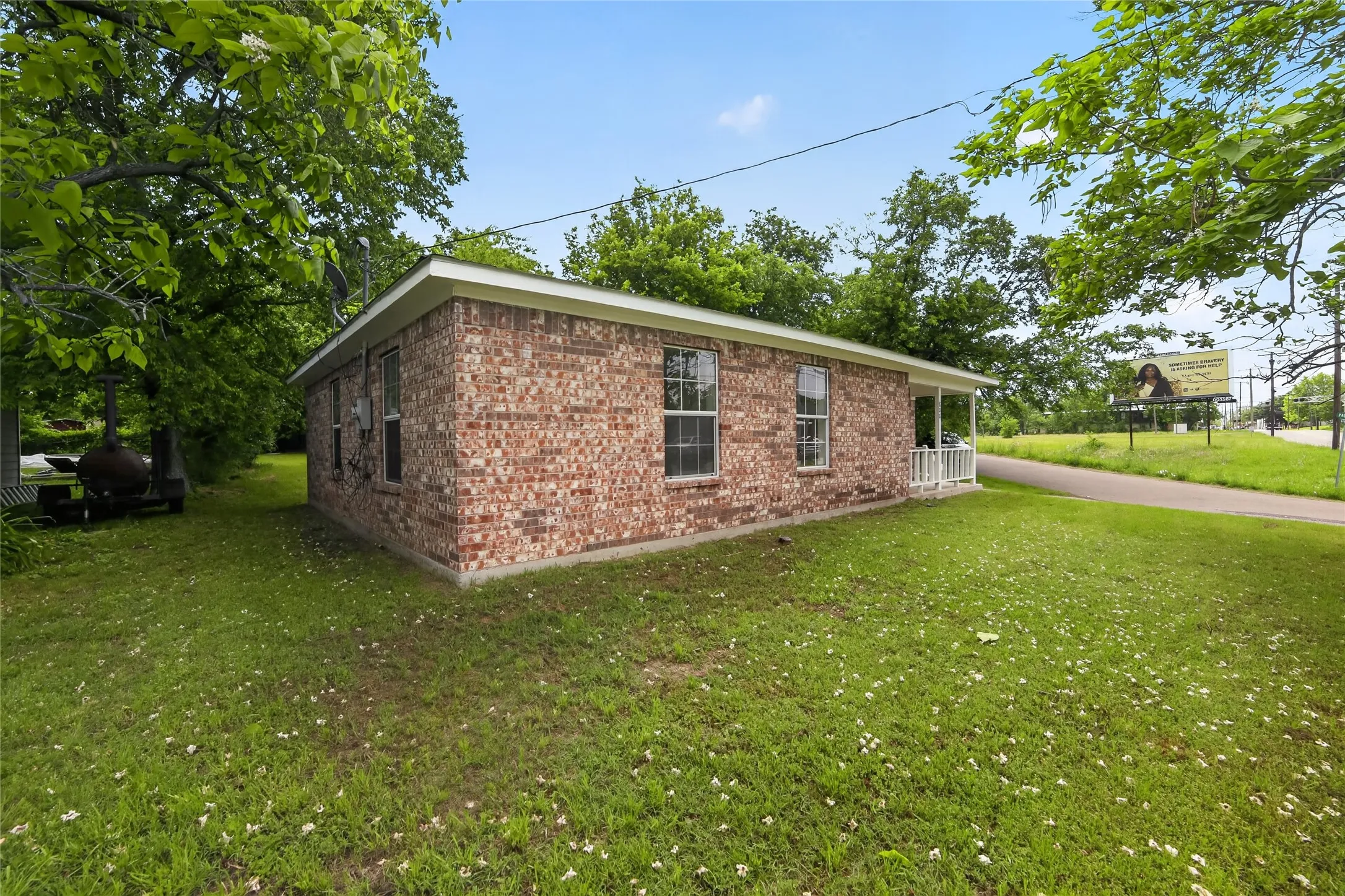This property features a brick exterior, a covered front porch with white railings, and an expansive lawn with mature trees