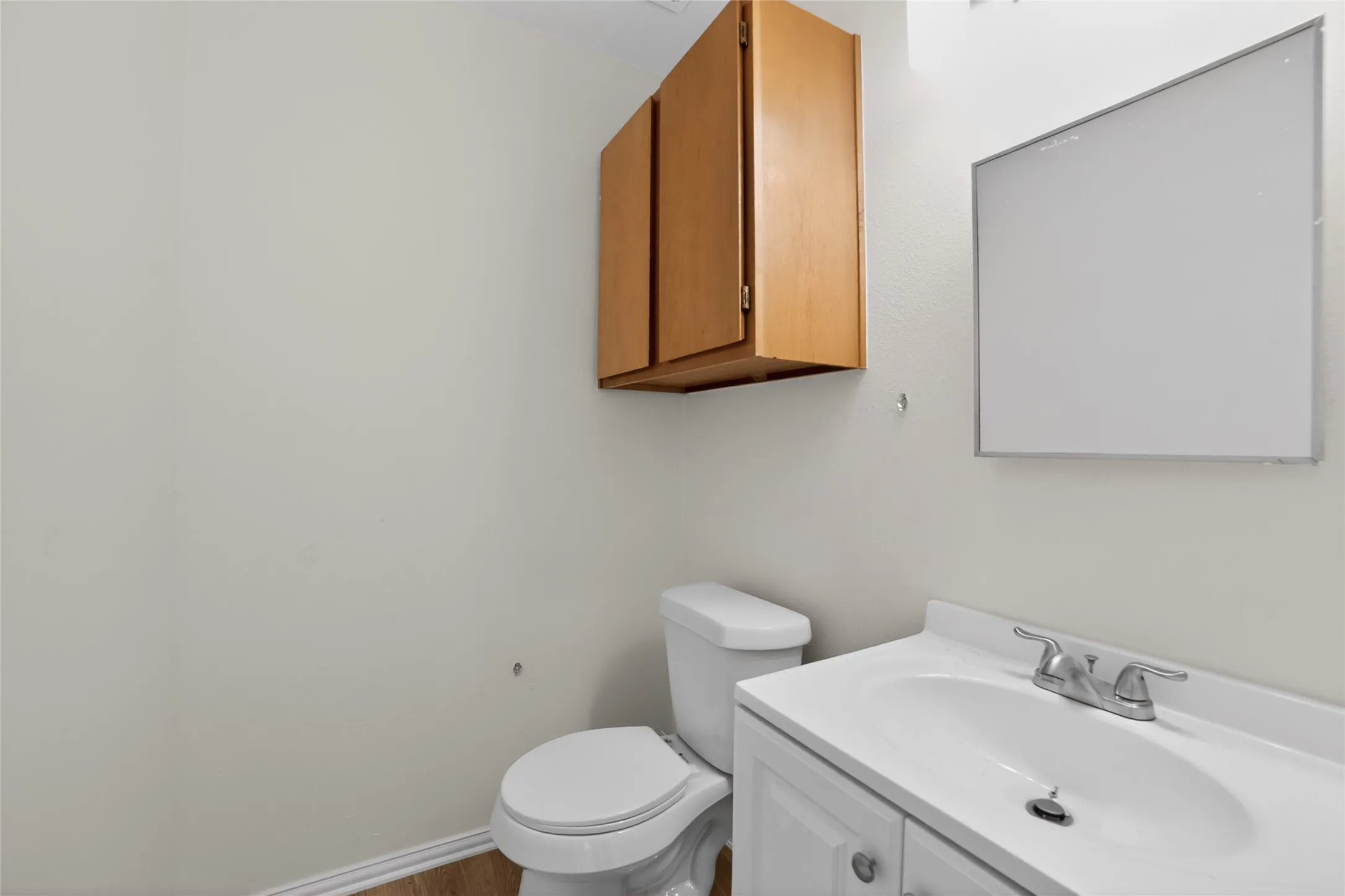 This bathroom features a white vanity with a sink and a chrome faucet, a white toilet, and a medicine cabinet with wooden doors