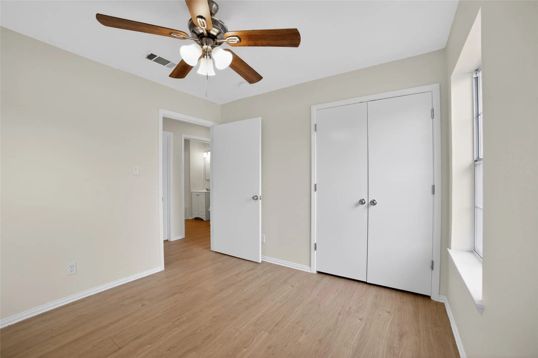 This room features wood-look flooring, a ceiling fan with light fixture, and a window providing natural light