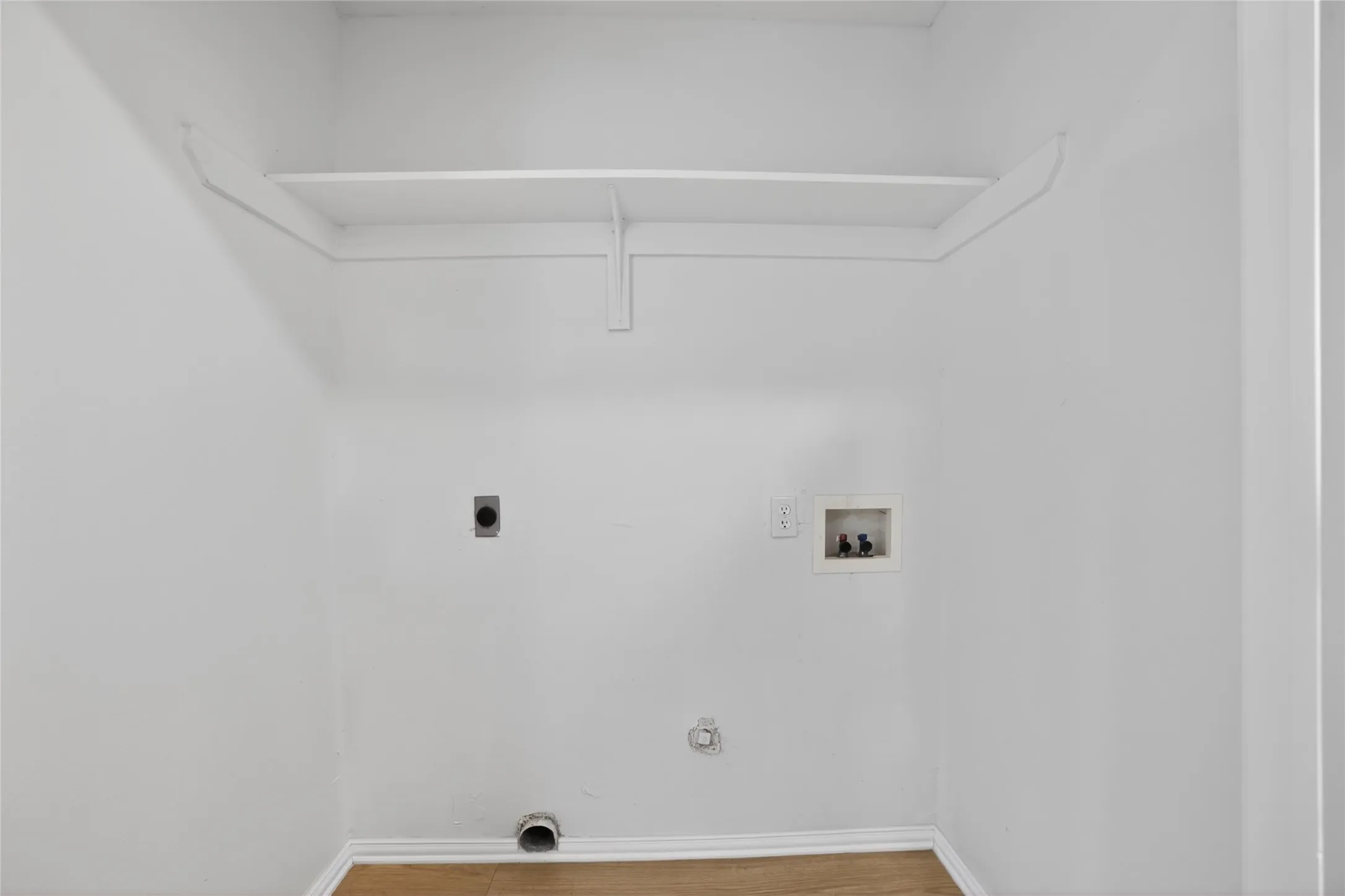 This utility area features light-colored walls, a built-in shelf, and wood flooring