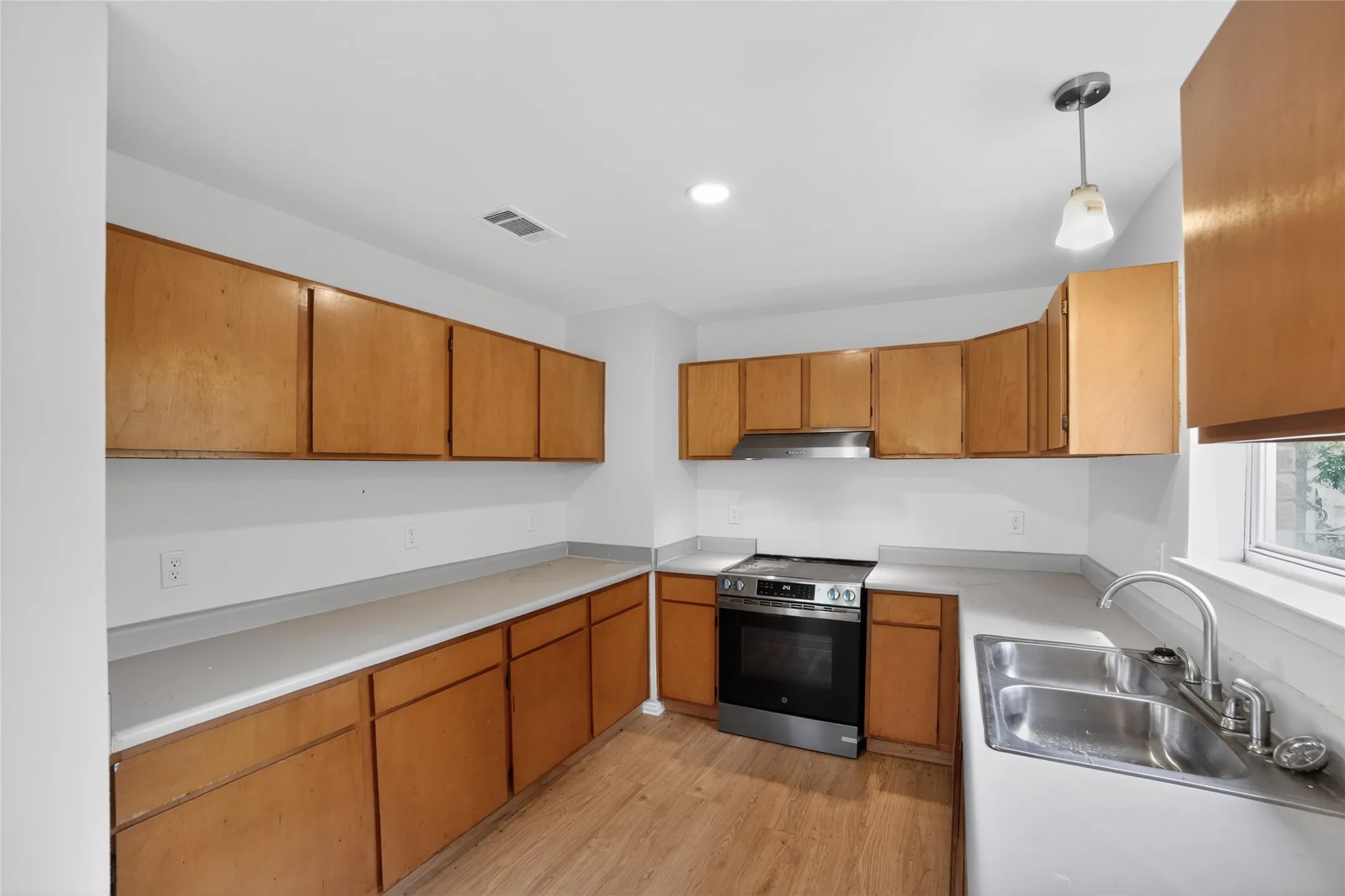 The kitchen features extensive wooden cabinetry, a stainless steel oven and range hood, and a double basin sink