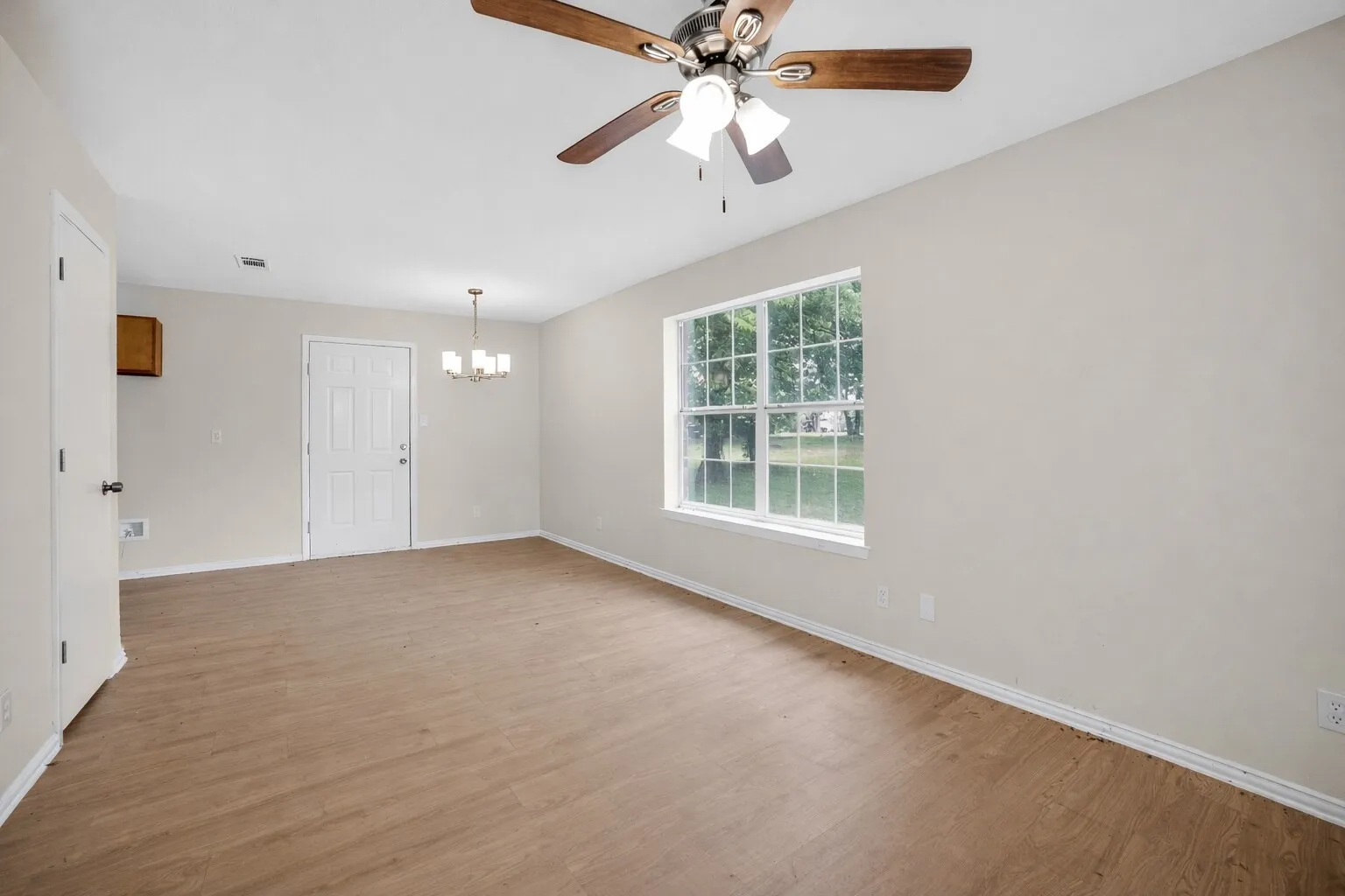 Spacious living area featuring light-colored walls, wood-look flooring, and a ceiling fan