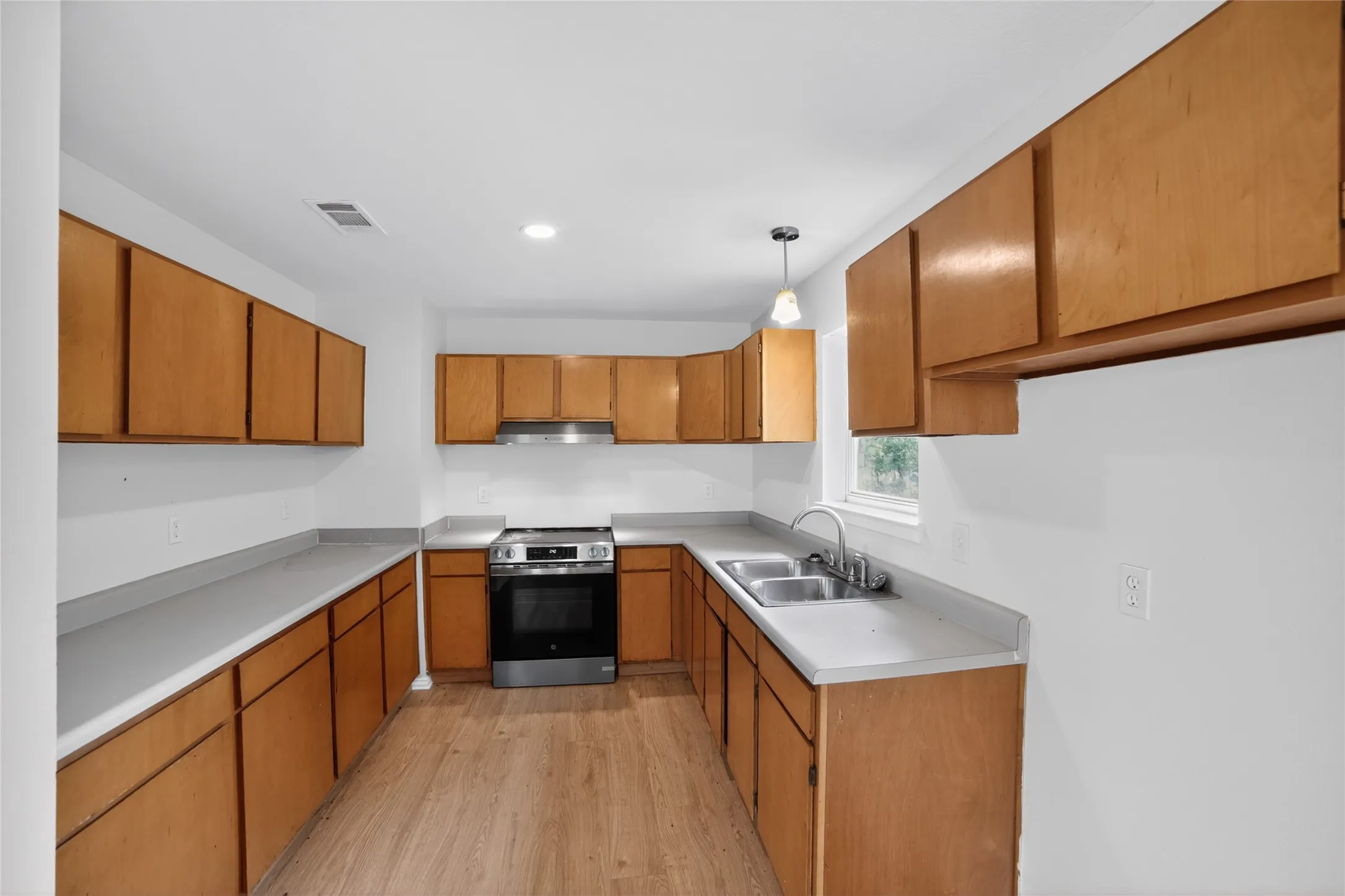 Kitchen featuring wood cabinetry, light-colored countertops, a stainless steel oven with an overhead range hood, and a double-basin stainless steel sink