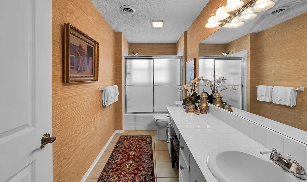 Hall bath convenient location featuring a double vanity with a white countertop, an integrated sink, and a large mirror with overhead lighting