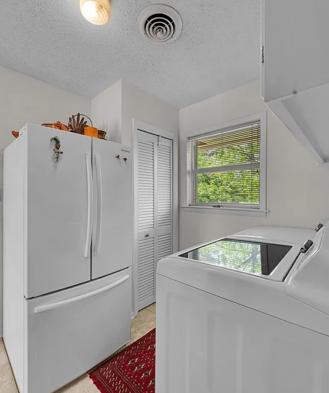 Utility room featuring a white refrigerator, a louvered bifold door, a window with blinds, and tile flooring