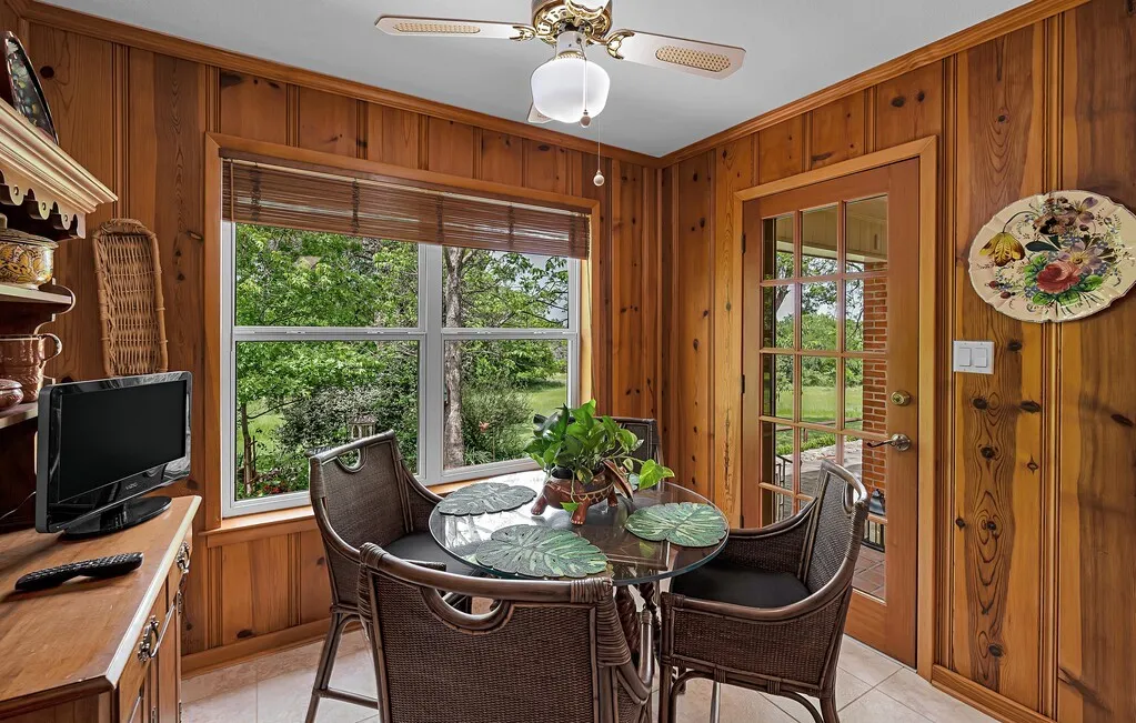 This dining area features wood paneling, a large window with outdoor views, and a glass-paned door,  just outside is a patio