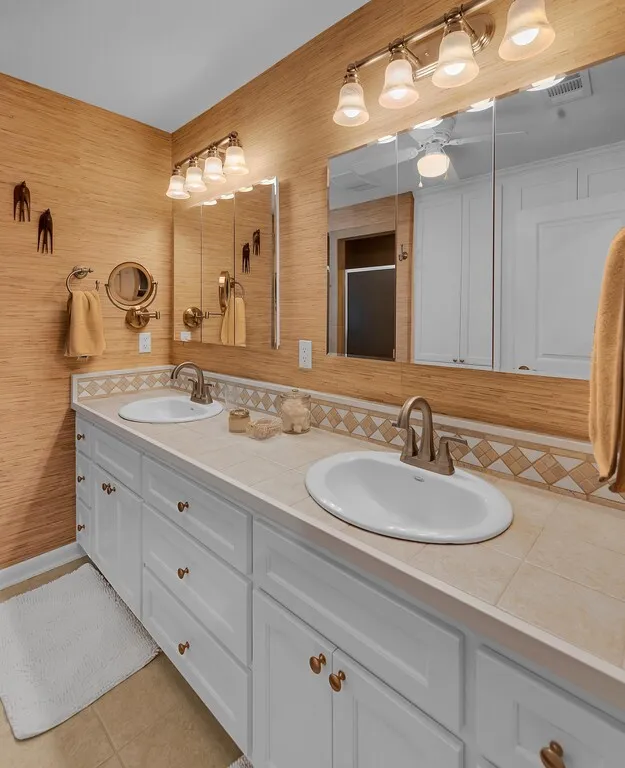 Bathroom vanity with two undermount sinks, bronze faucets, and white cabinetry with bronze hardware