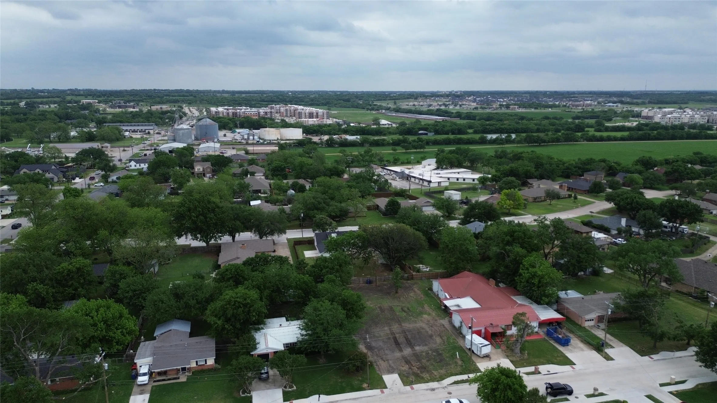 Aerial view of the surrounding neighborhood with established trees, residential properties, and open green spaces