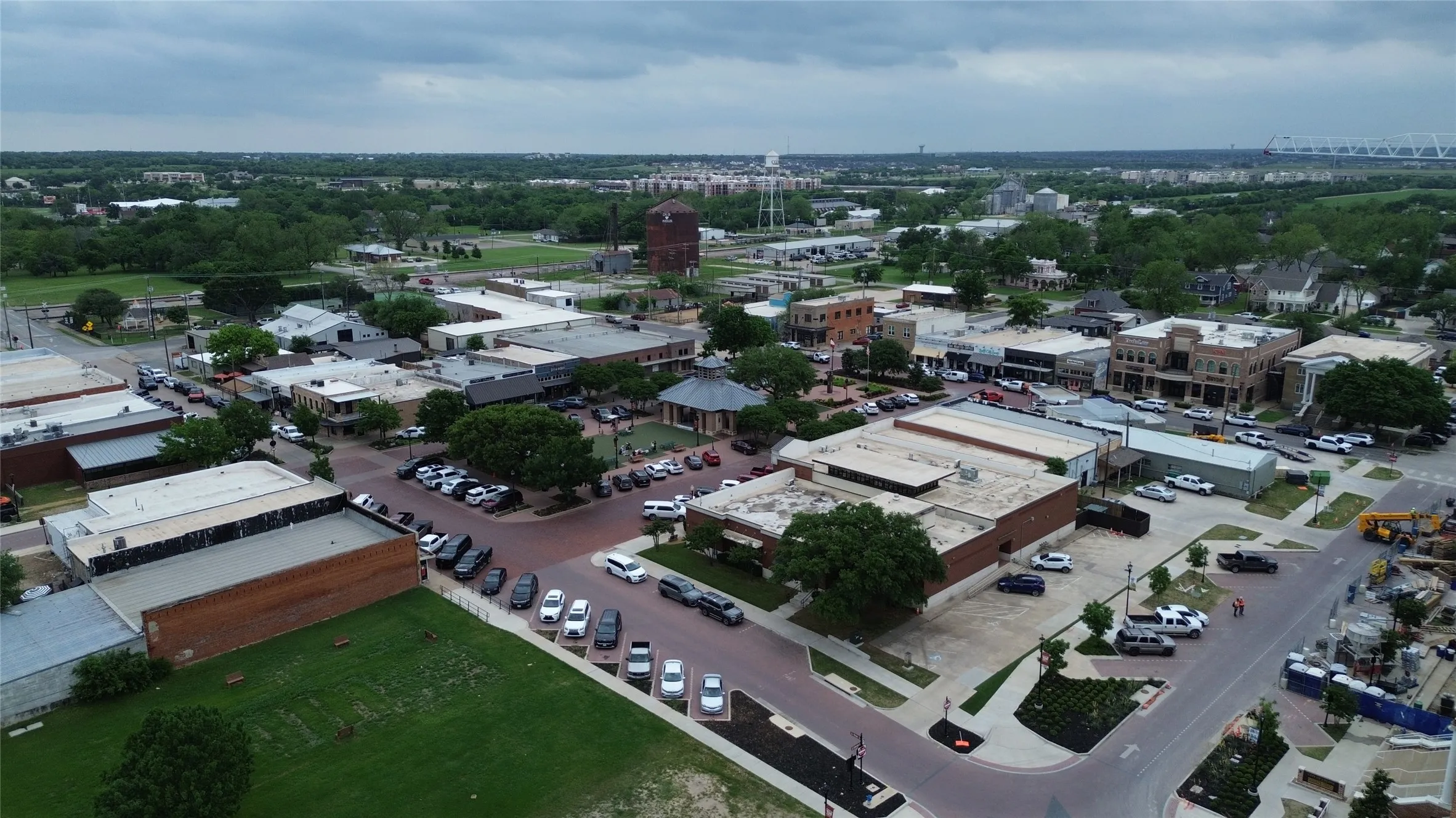 An aerial view of the community, featuring commercial buildings, parking areas, and mature trees, with a large water tower visible in the distance
