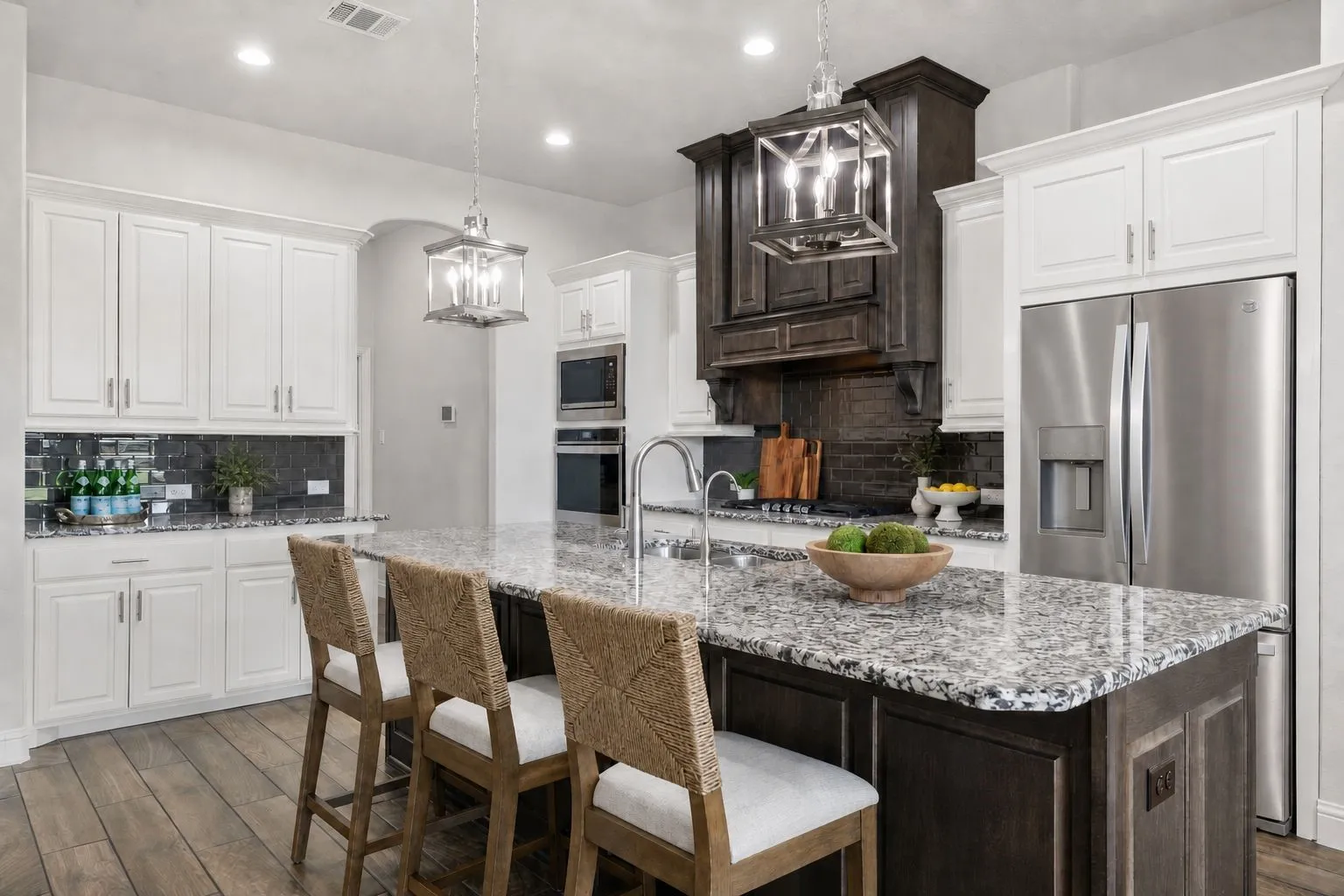 Open-concept kitchen featuring an oversized island with seating, granite countertops, stainless steel appliances, wood-finish flooring, and pendant lighting fixtures
