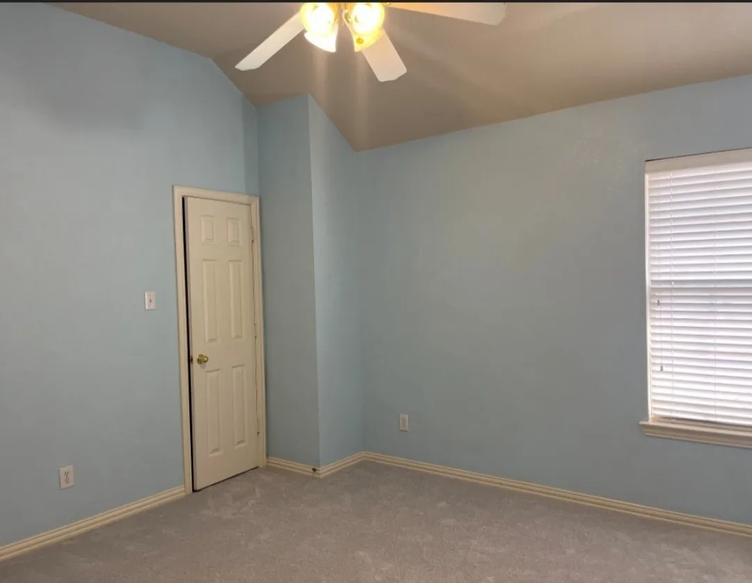Spacious interior room featuring light blue walls, gray carpet flooring, and white baseboards