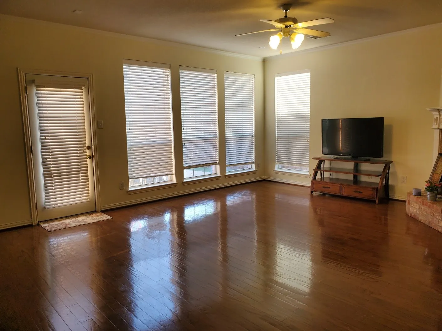Spacious room featuring wood-finish flooring, a ceiling fan with integrated lighting, and multiple windows with blinds