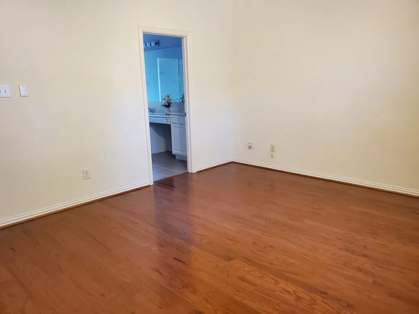 Polished wood-finish flooring extending into a bright interior with white baseboards and walls
