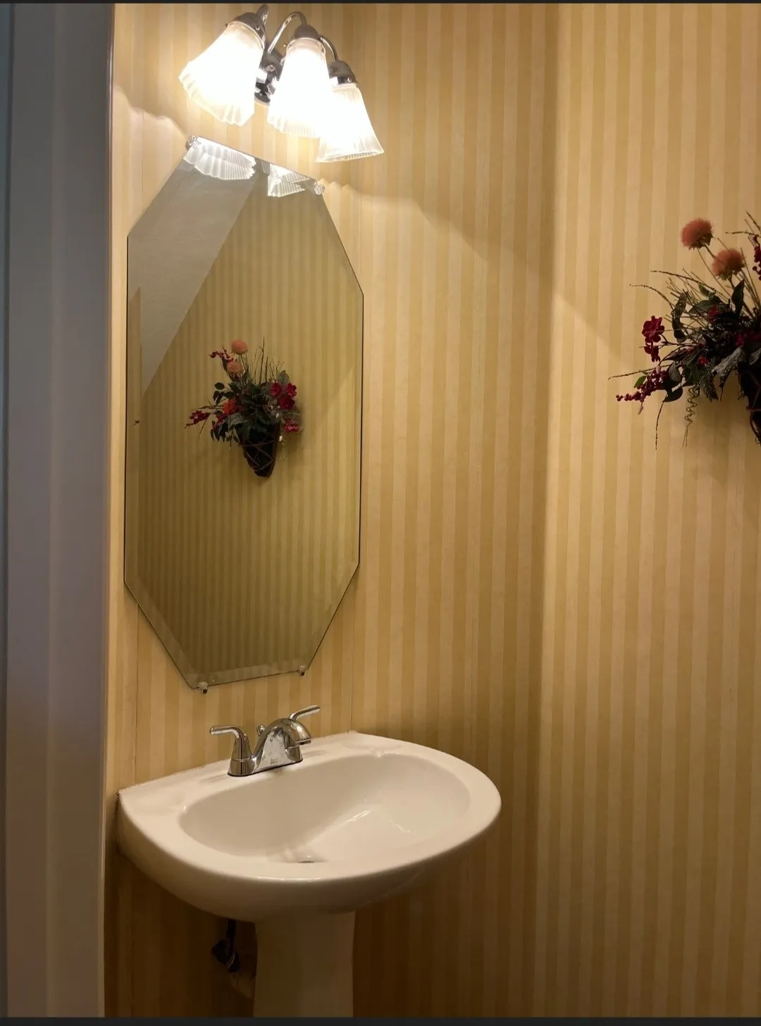 Pedestal sink with chrome faucet hardware, set against striped wallpaper