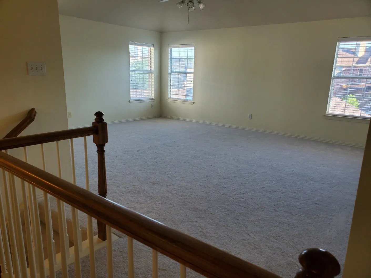 Expansive carpeted room featuring multiple windows with horizontal blinds, a ceiling fan with integrated lighting, and a neutral wall color