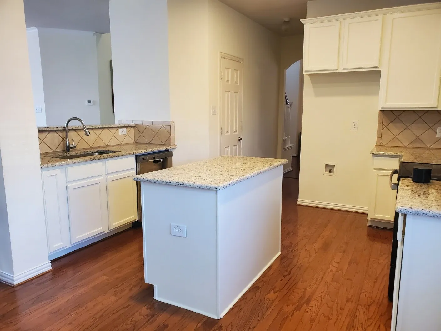 Kitchen featuring wood-finish flooring, white cabinetry, granite countertops, and a tile backsplash