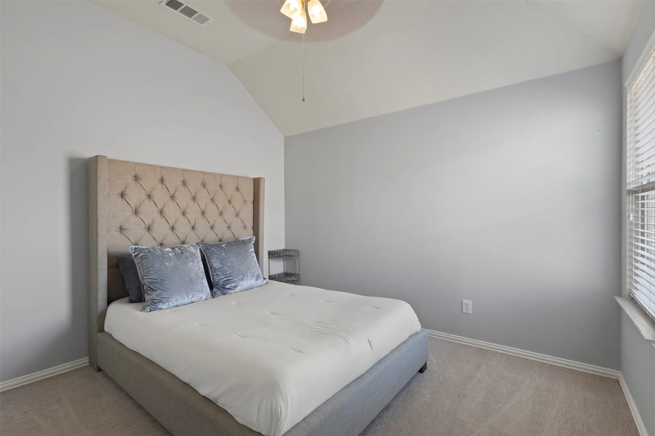This room features a vaulted ceiling with a ceiling fan, light gray walls, and carpeted flooring