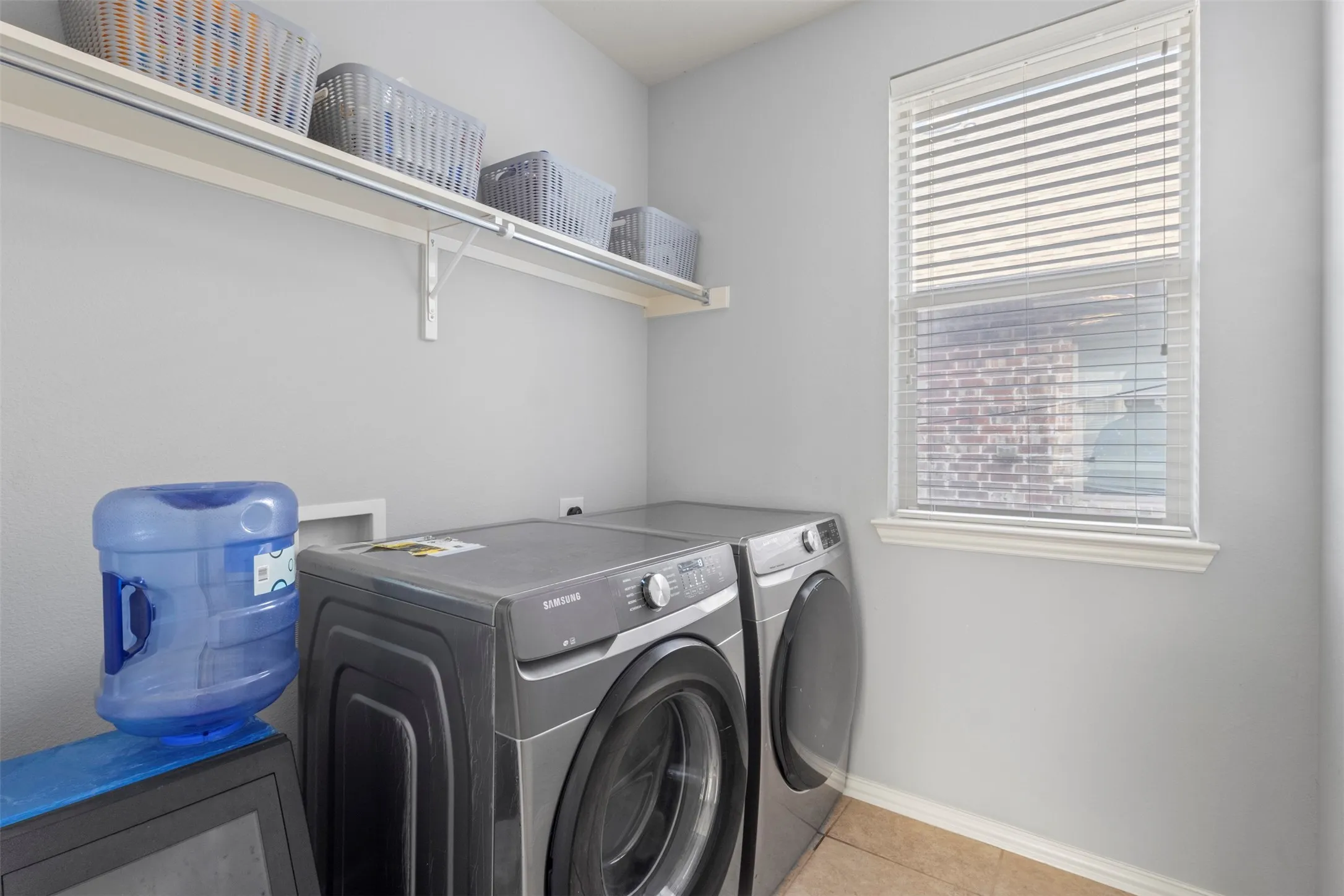 Laundry area featuring a window with blinds, a wall-mounted shelf, and ceramic tile flooring