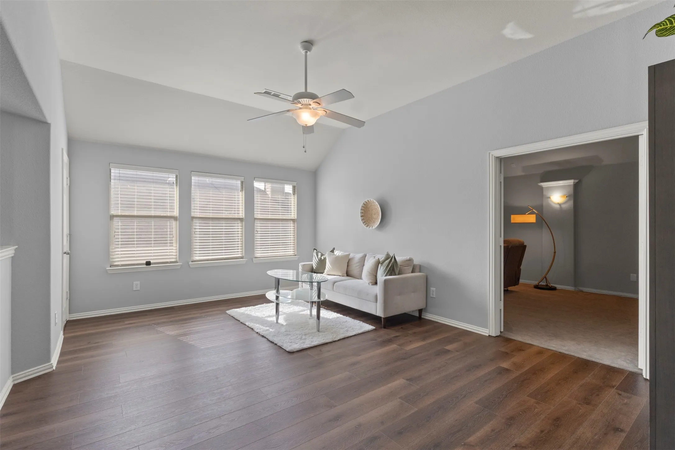Living room featuring dark wood style flooring, light gray walls, a vaulted ceiling, and three windows providing natural light