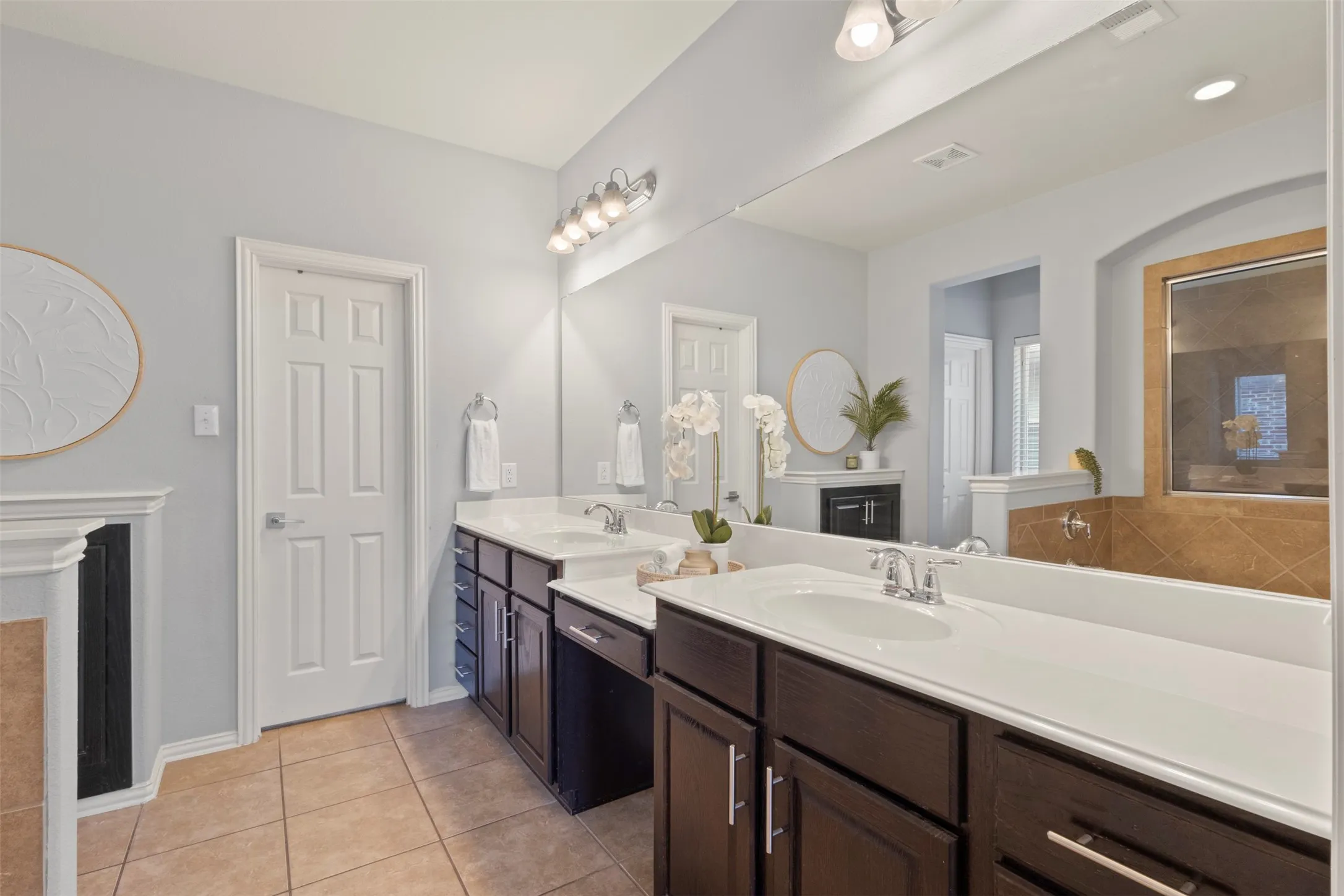 Bathroom featuring dual vanities with white countertops and dark wood cabinetry, a large wall mirror, and tile flooring
