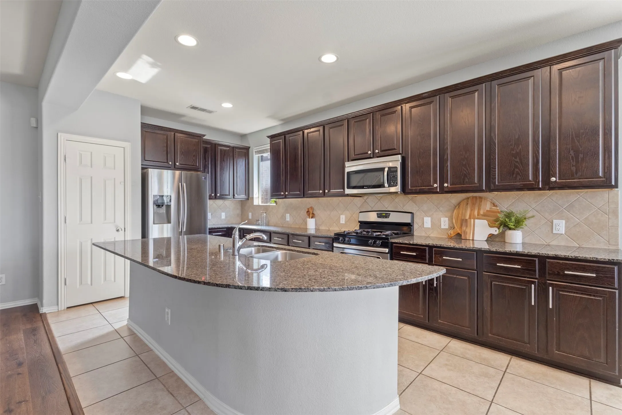 Well-appointed kitchen featuring an island with a sink, extensive dark wood cabinetry, stainless steel appliances, and tile flooring