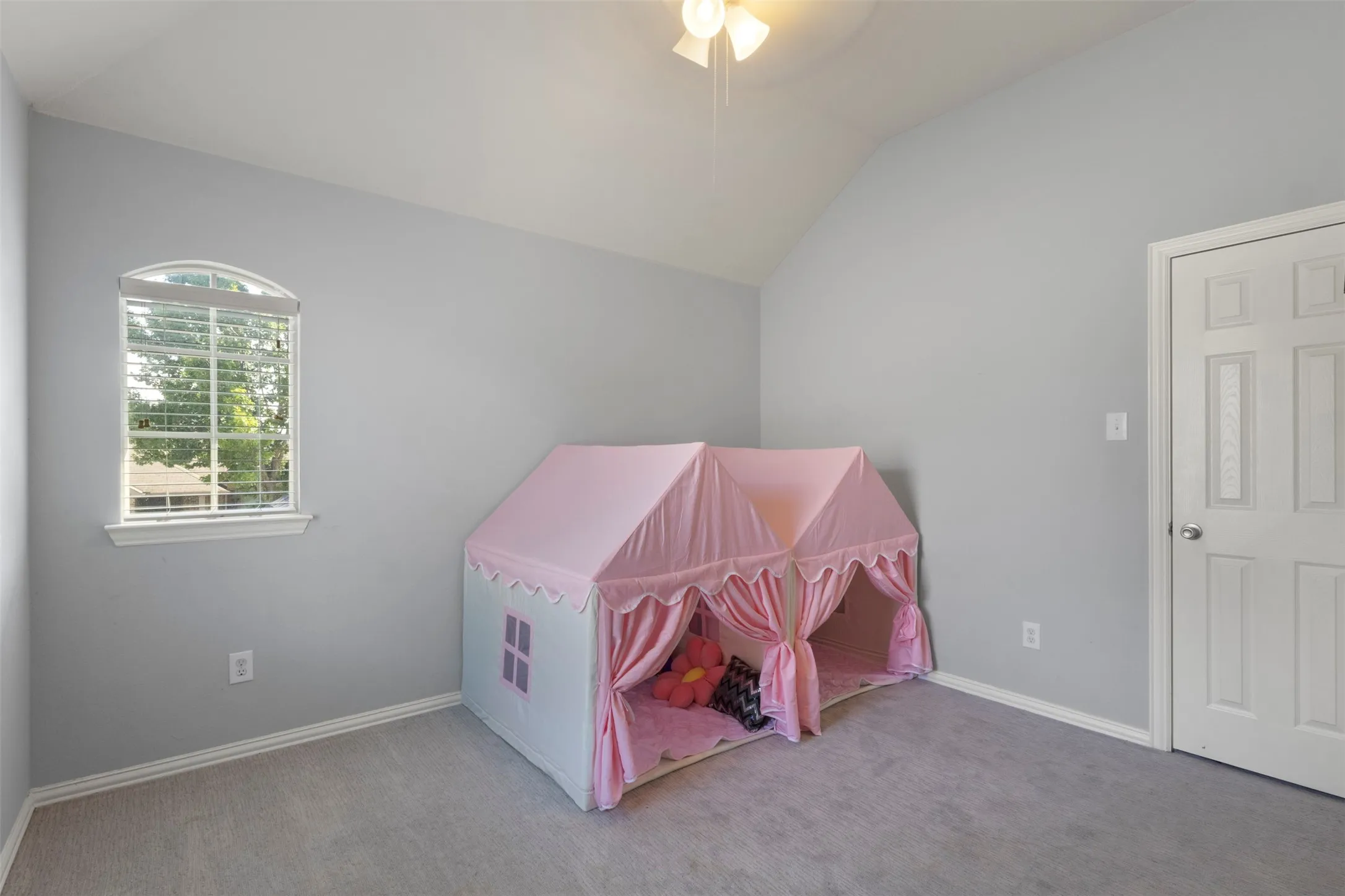 This room features a vaulted ceiling, light gray walls, and gray carpeting