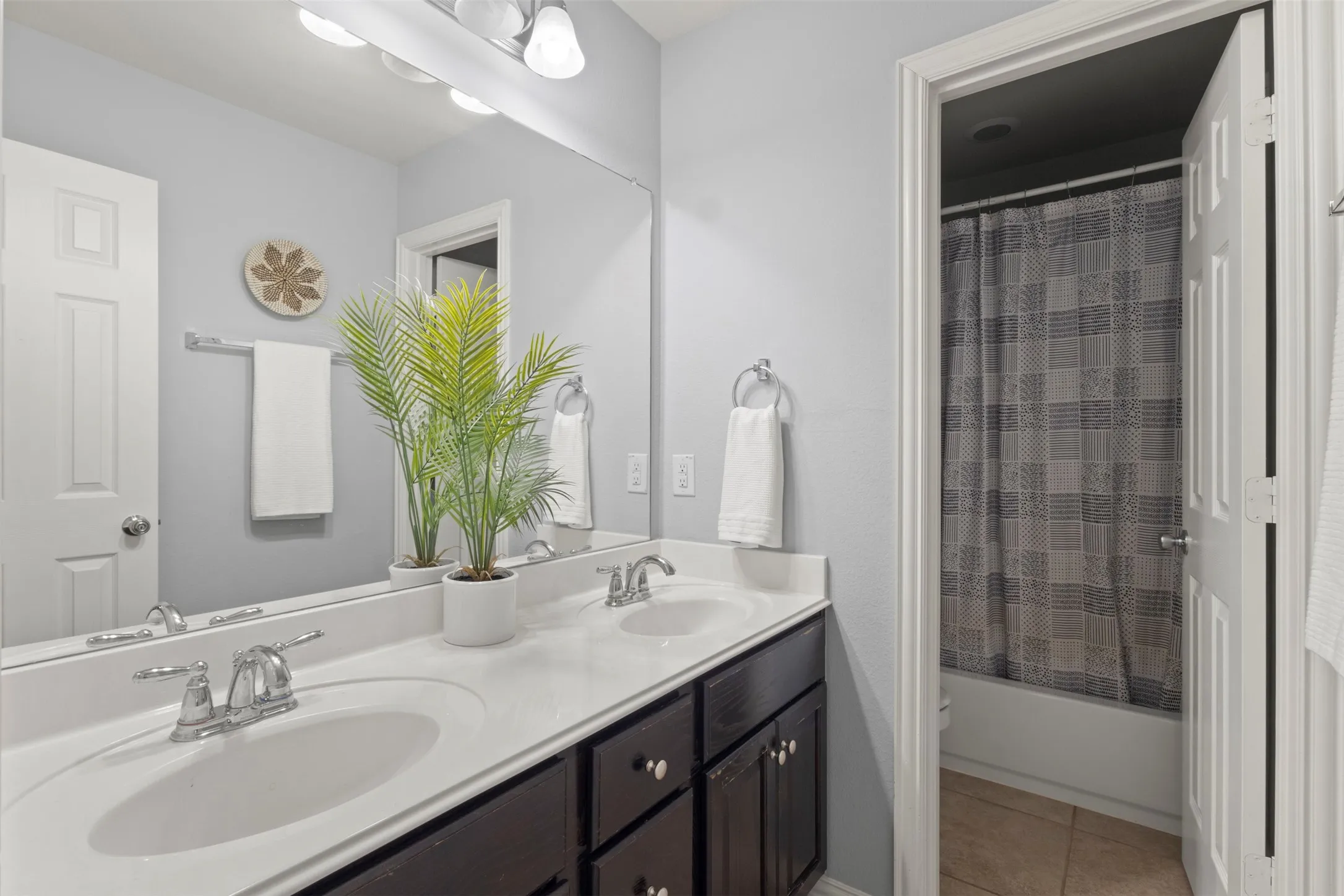 Bathroom featuring a double vanity with two sinks, dark wood cabinetry, and a spacious mirror